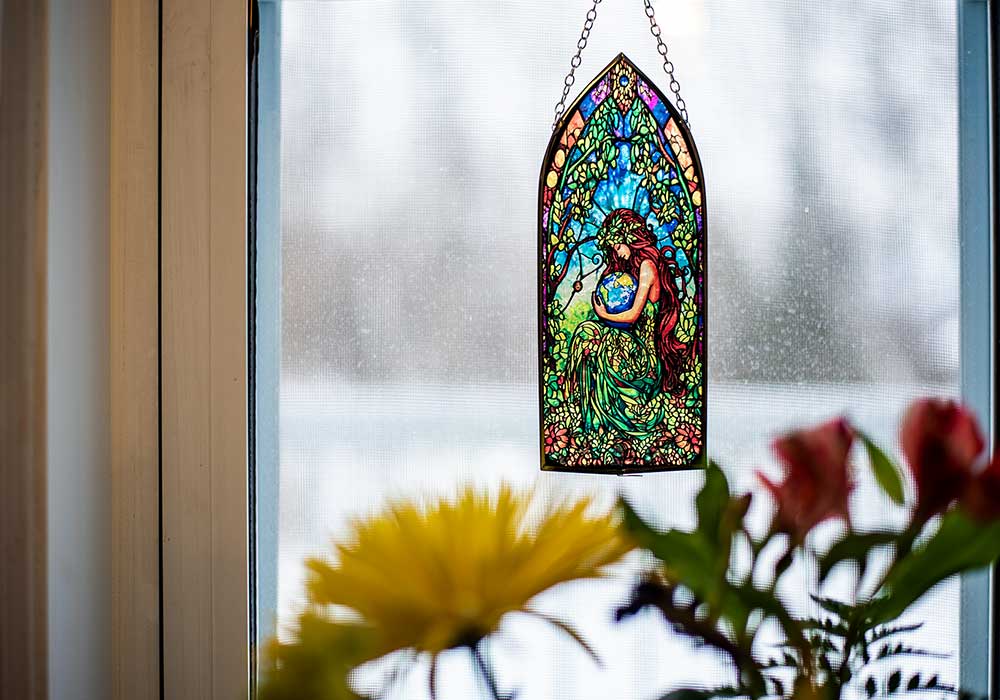 Colorful stained glass window hanging on a window with flowers in the foreground