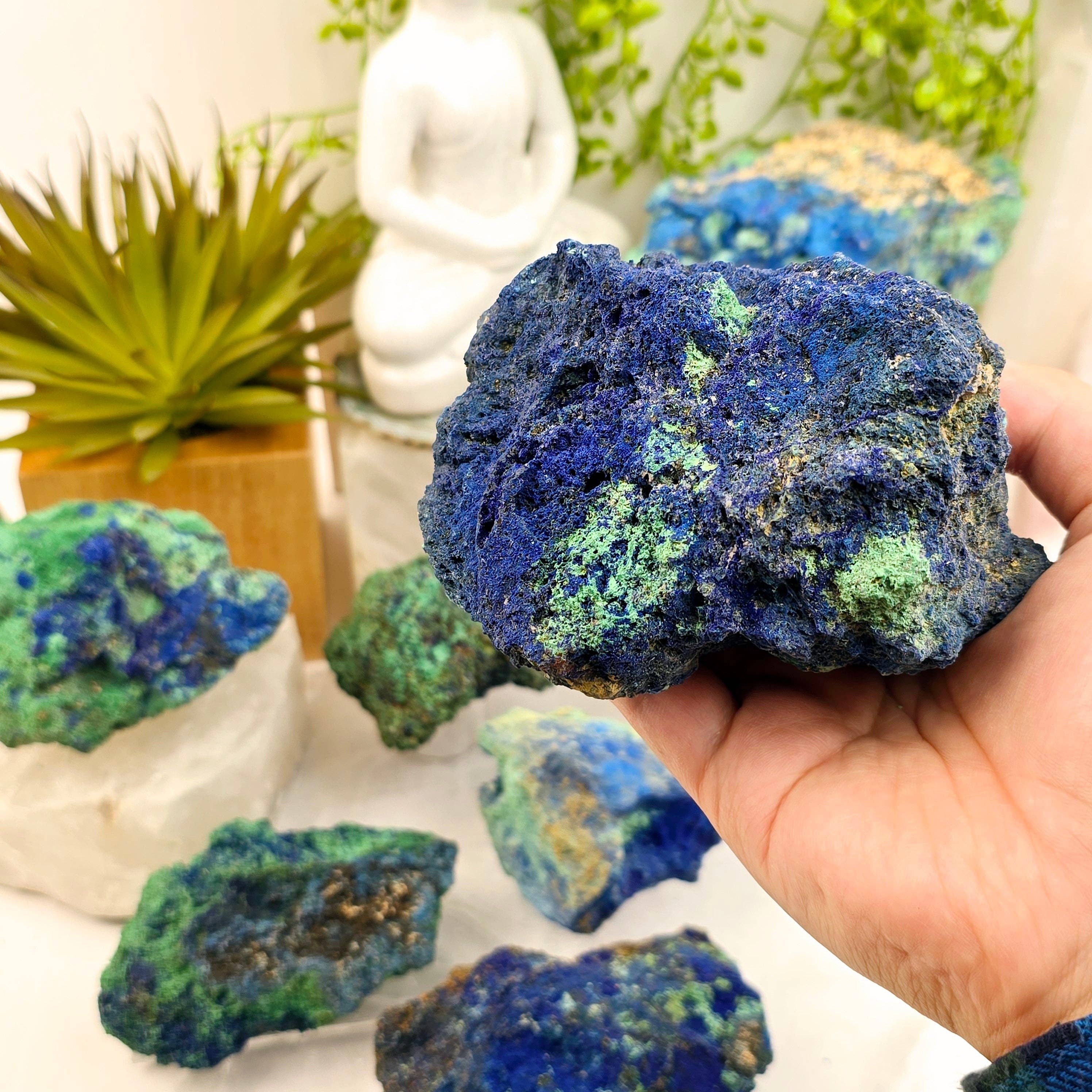 Hand holding a blue and green mineral specimen with a blurred indoor setting