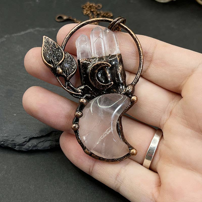 Hand holding a decorative pendant with crystal-like stones on a dark surface