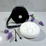 White handpan with black handle and purple flowers on a light gray surface