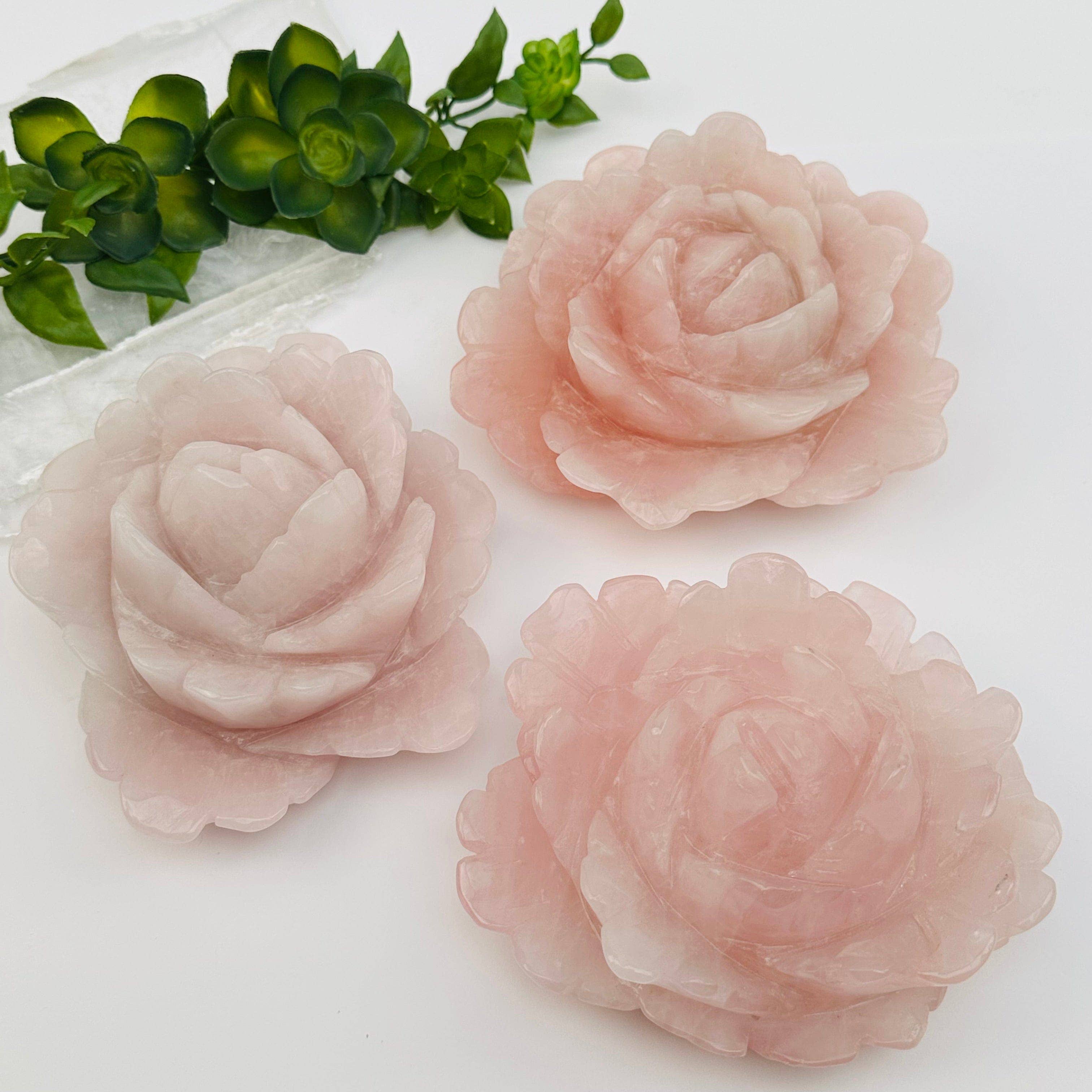 Three pink artificial roses on a white surface with green leaves in the background.