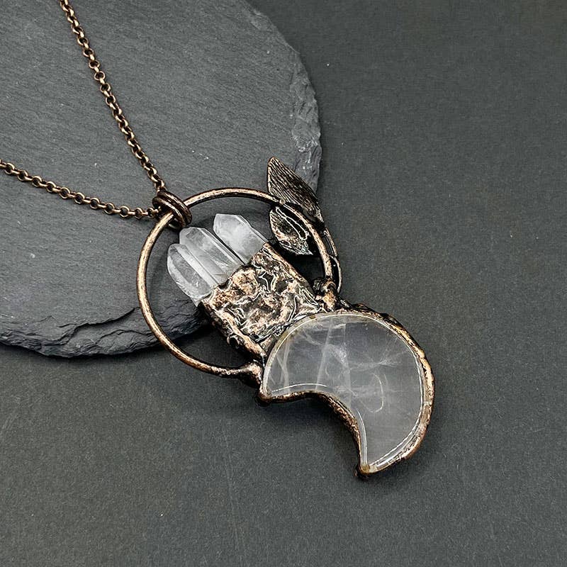 Necklace with a unique pendant featuring a crystal and leaf design on a dark surface.