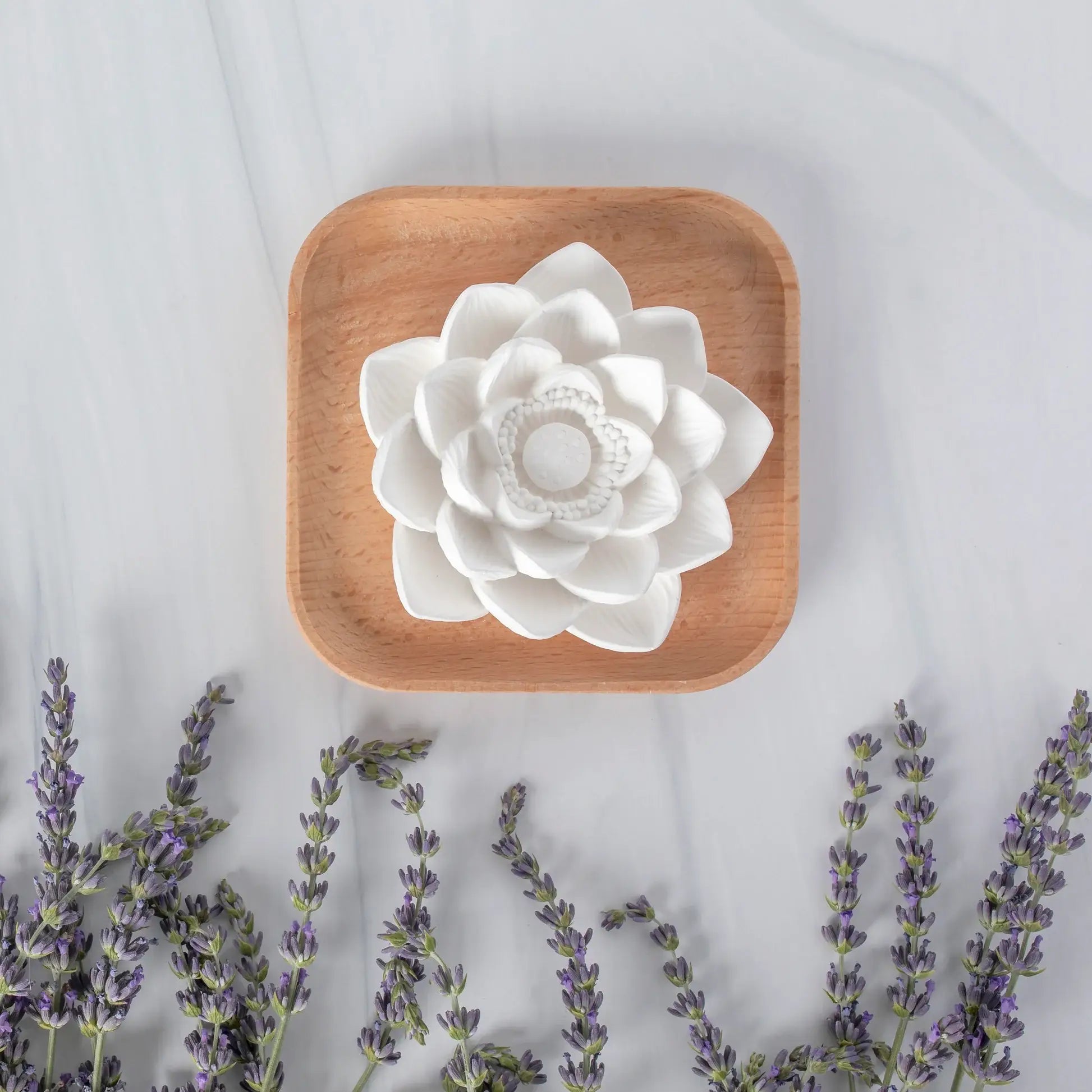 White ceramic flower on a wooden plate with lavender flowers on a light background