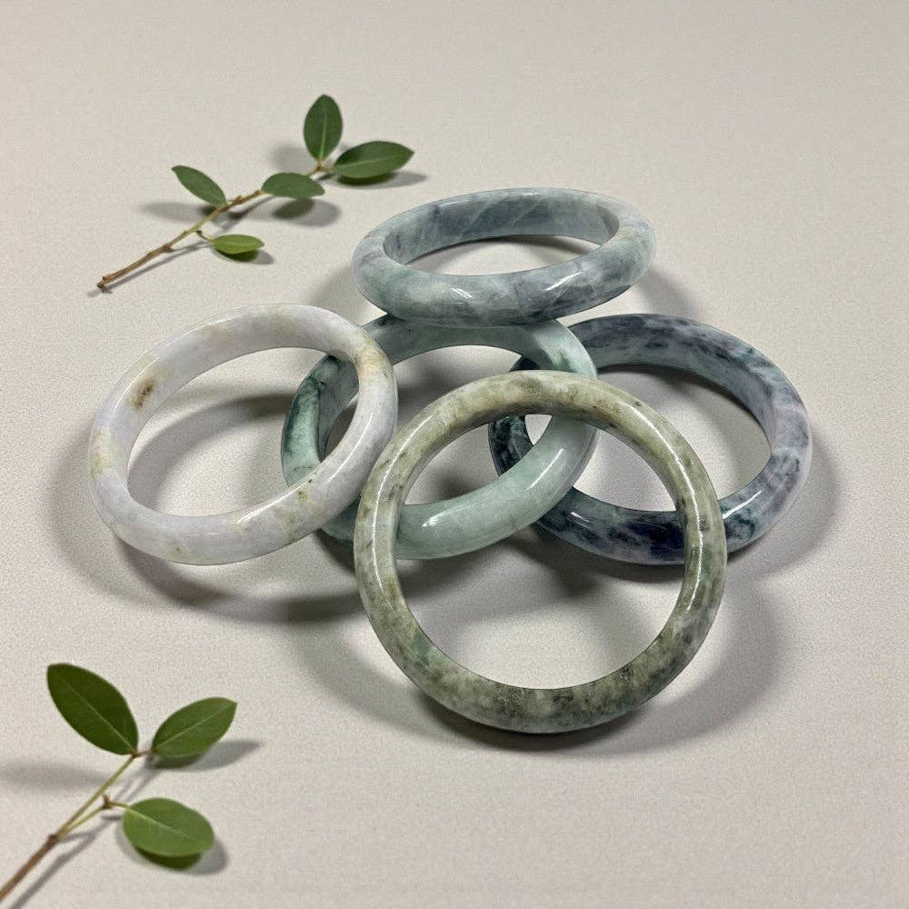 Stack of jade bracelets on a neutral background with green leaves.