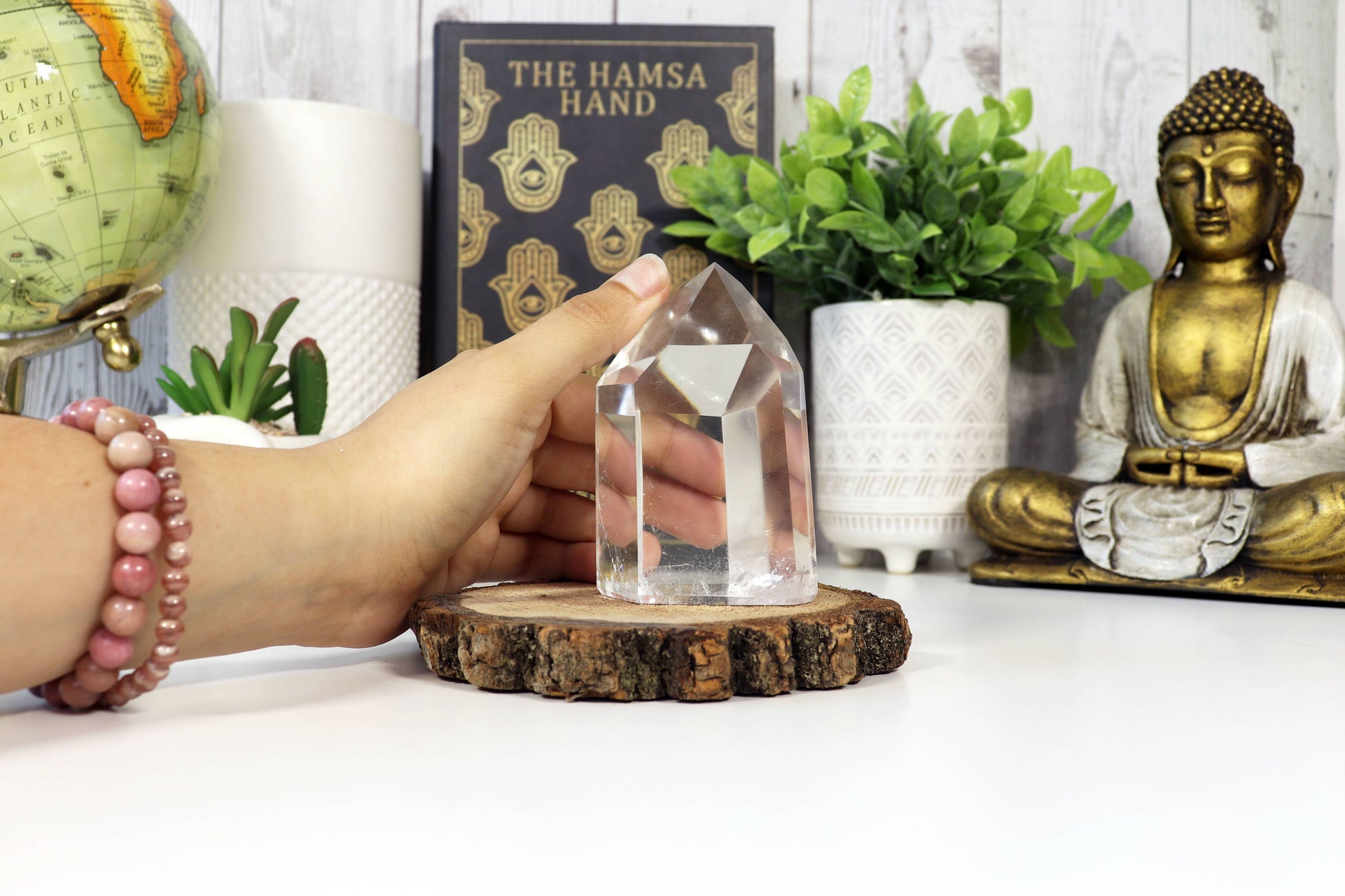 Person holding a crystal object on a wooden base with decor items including a Buddha statue and a globe.