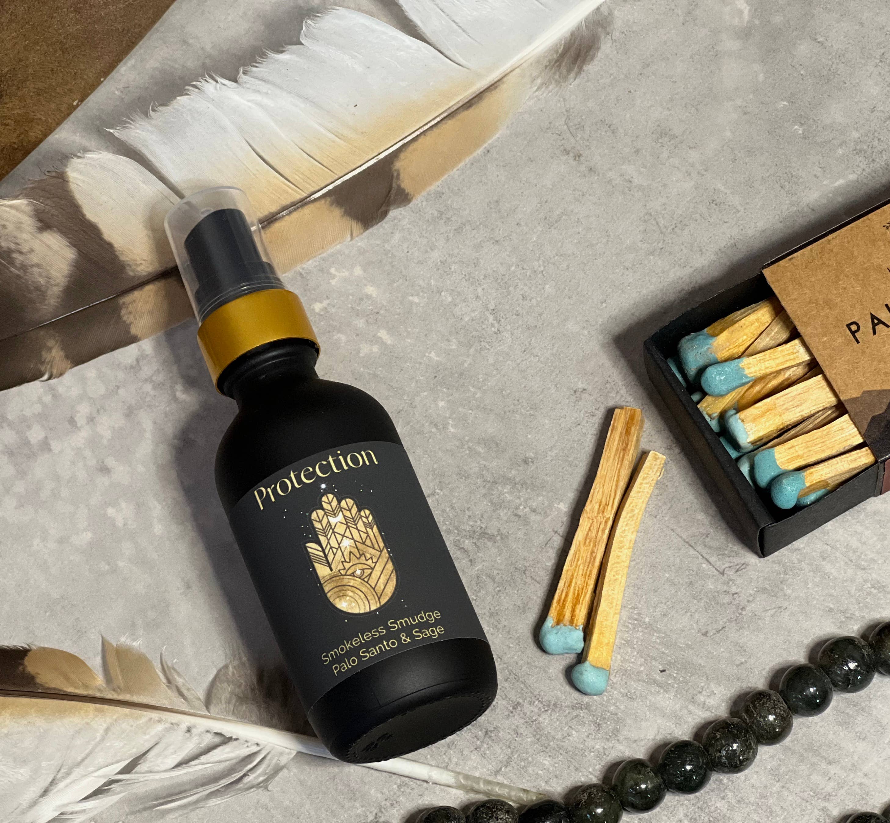 Black bottle labeled 'Protection' with matches and feathers on a textured surface