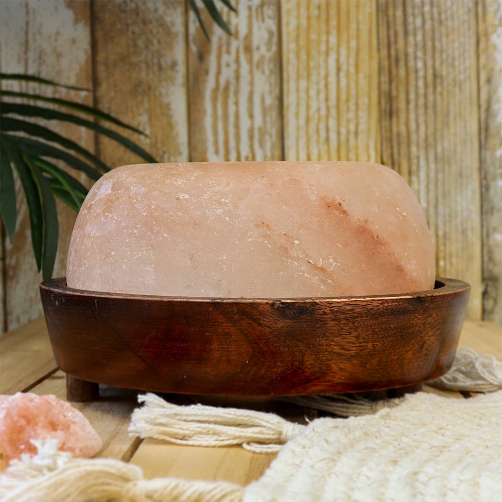 Himalayan salt lamp in a wooden base on a wooden surface with a natural background