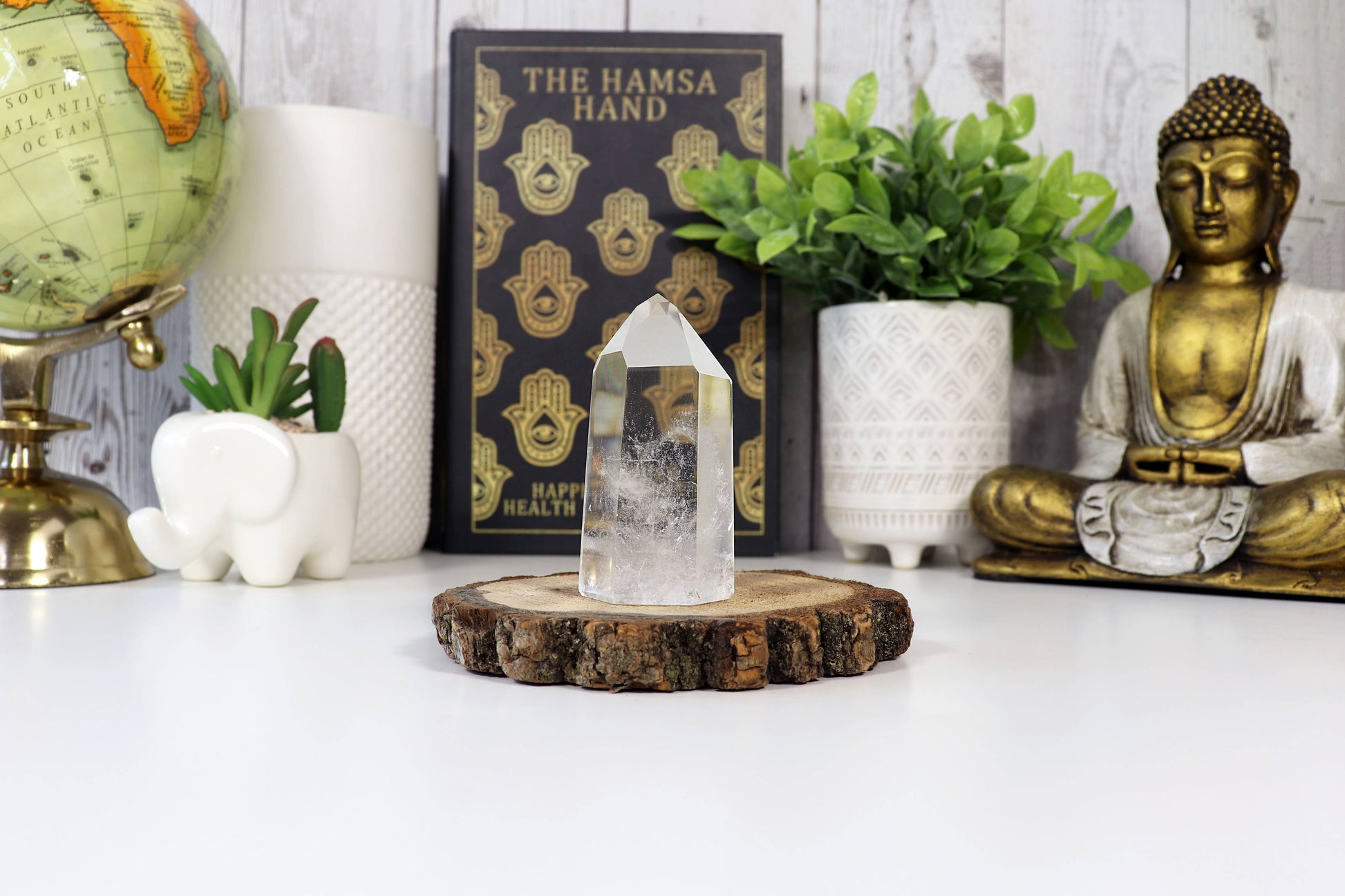 Decorative setup with a crystal on a wooden stand, Buddha statue, and plants.