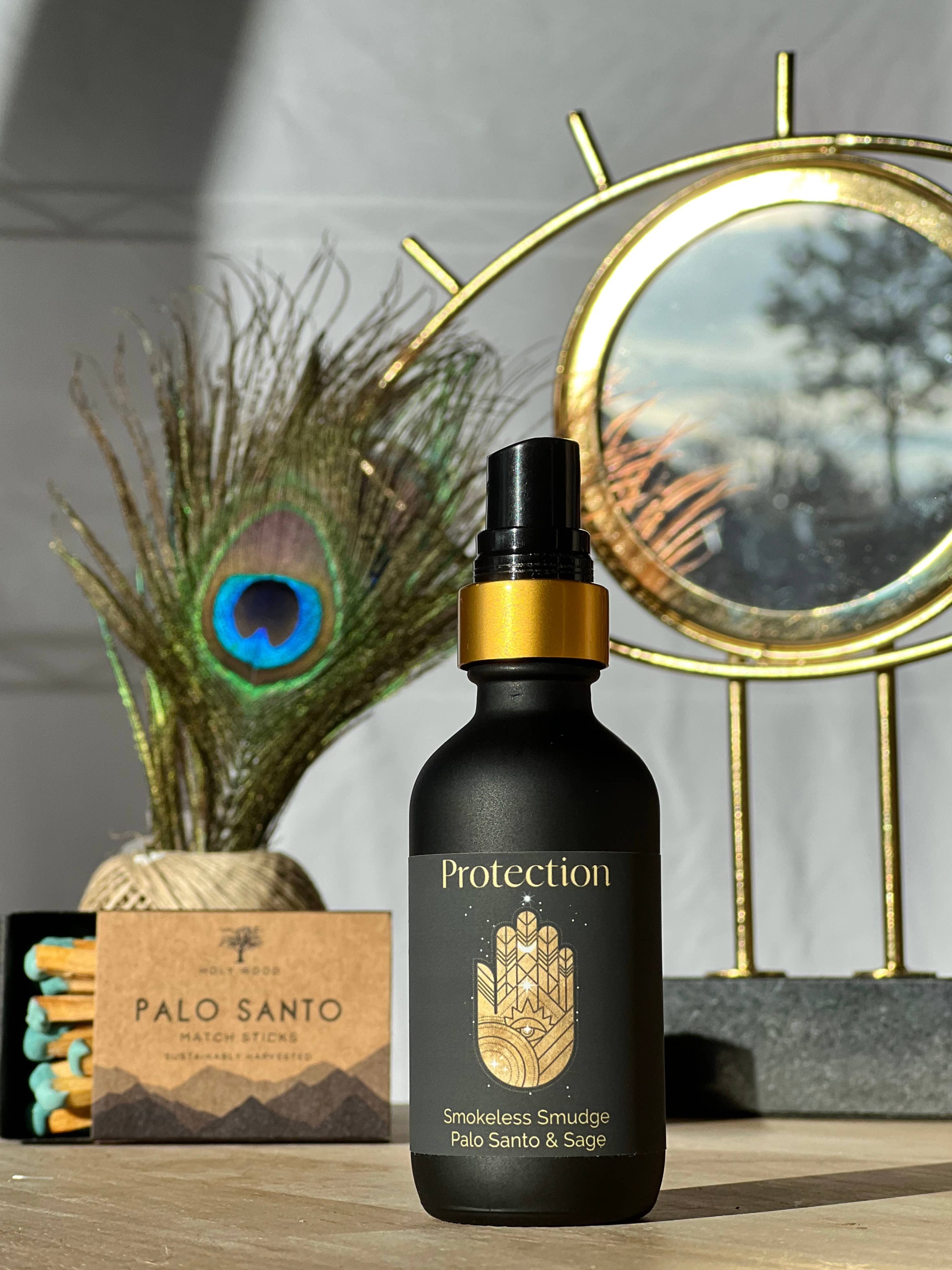 Black bottle labeled 'Protection' with a gold cap on a wooden surface, peacock feather and mirror in the background.
