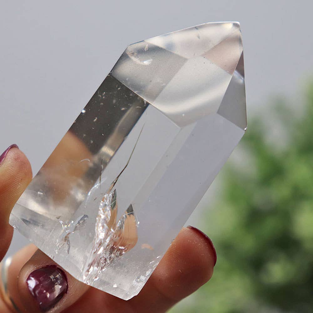 Clear crystal held by a hand with blurred greenery in the background