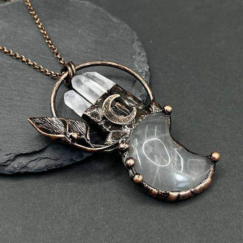 Necklace with a crescent moon and leaf design on a dark stone surface