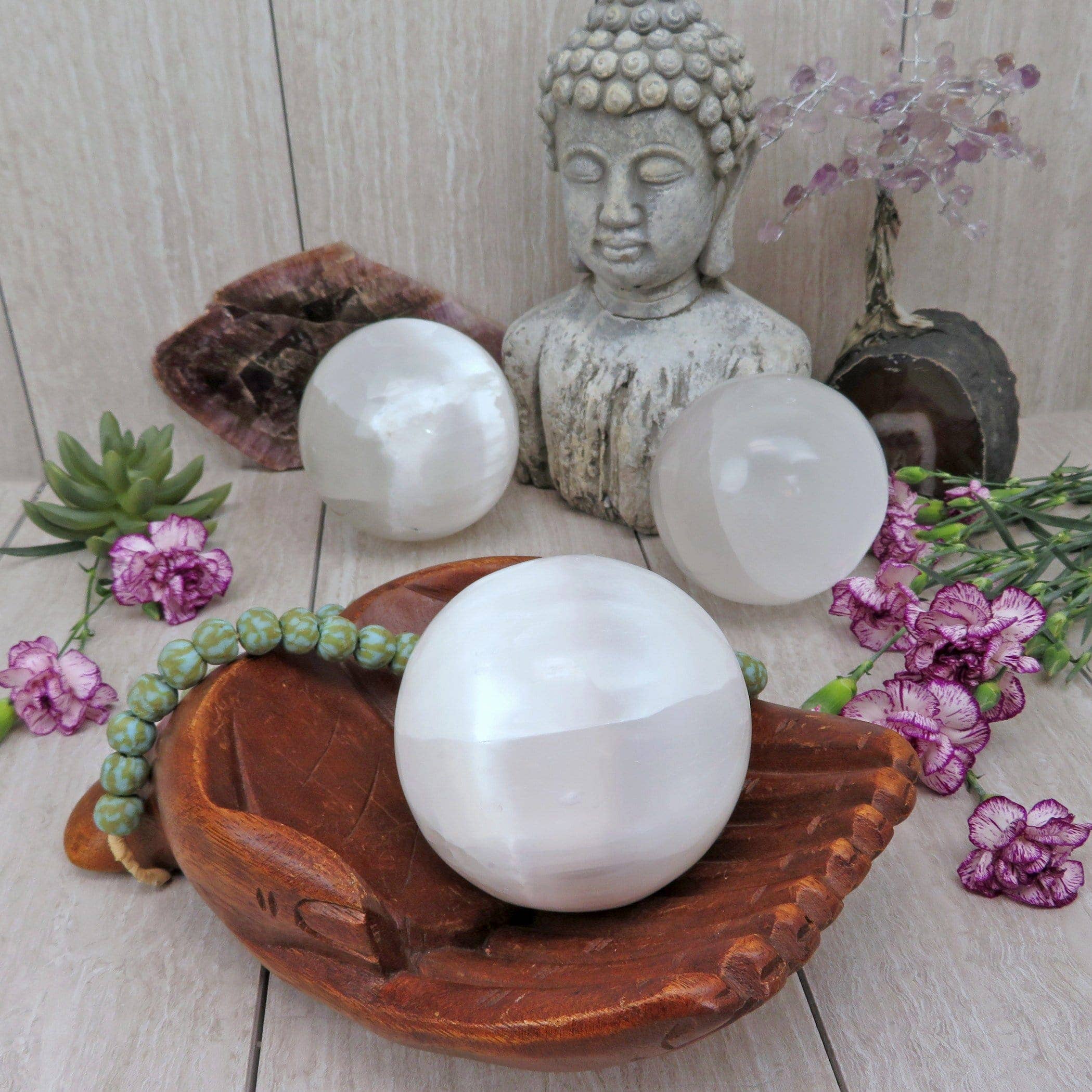White crystal balls on a wooden dish with a Buddha statue and flowers in the background