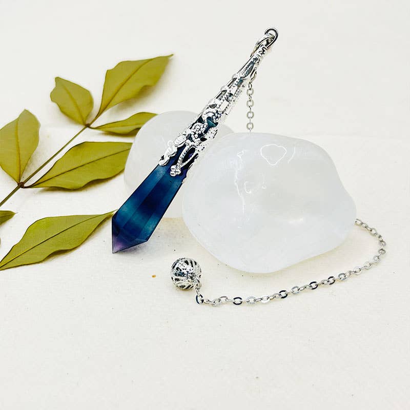Crystal wand with blue tip and silver chain on a white base with green leaves.