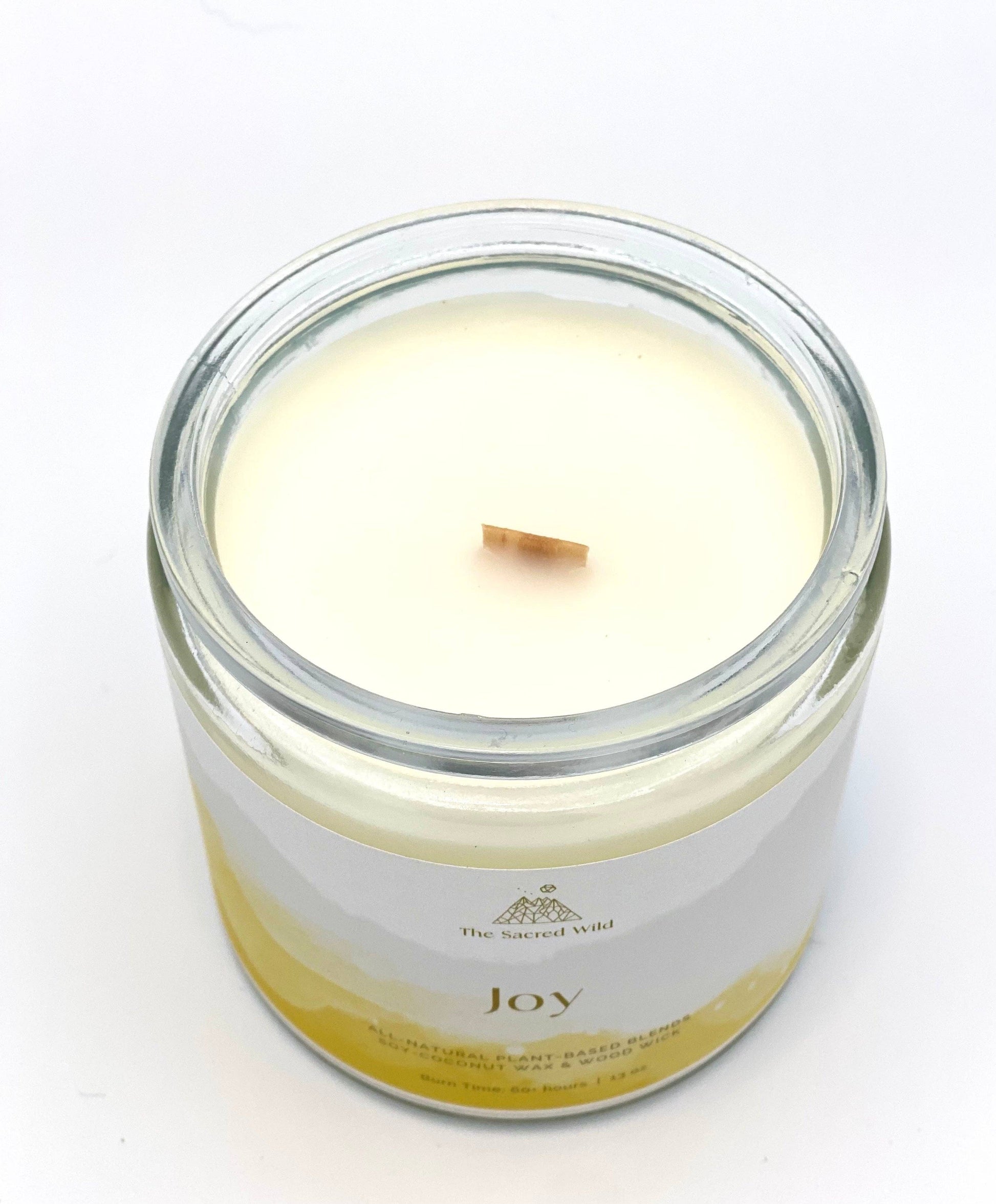 Candle in a glass jar labeled 'Joy' on a white background