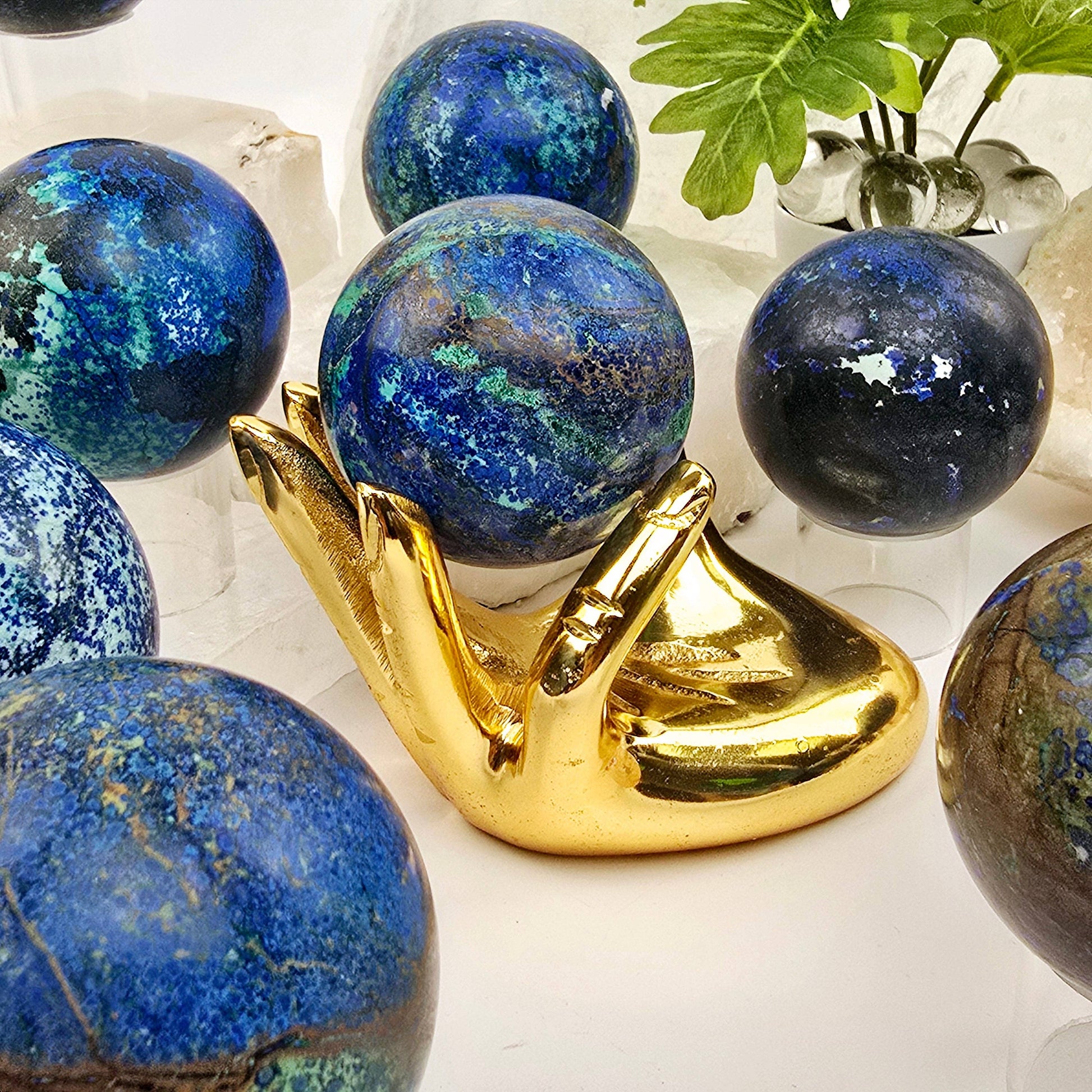 Blue marbled spheres on a gold stand with a plant in the background