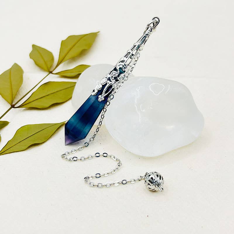 Decorative item with a blue crystal and silver chain on a white surface with green leaves.