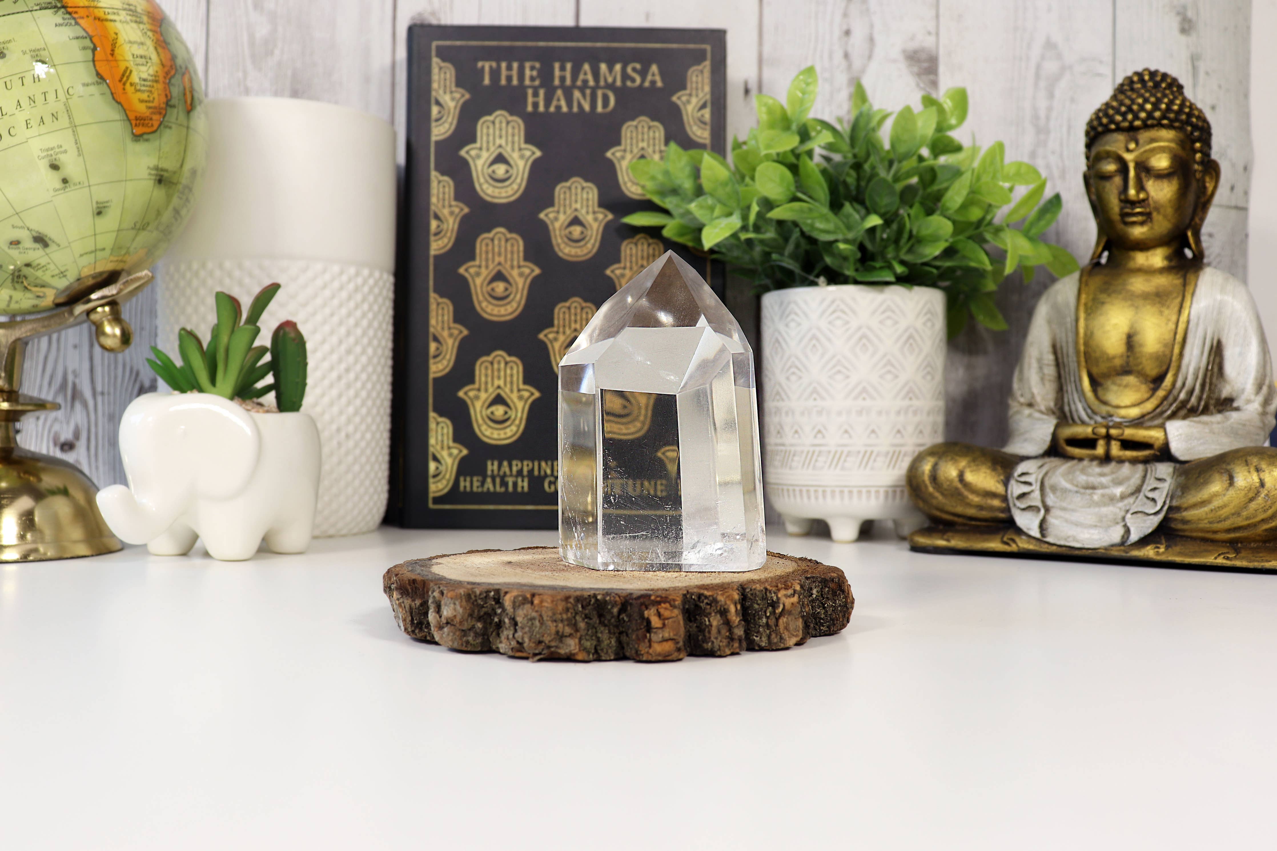 Decorative setup with a crystal, books, plants, and a Buddha statue on a wooden surface.