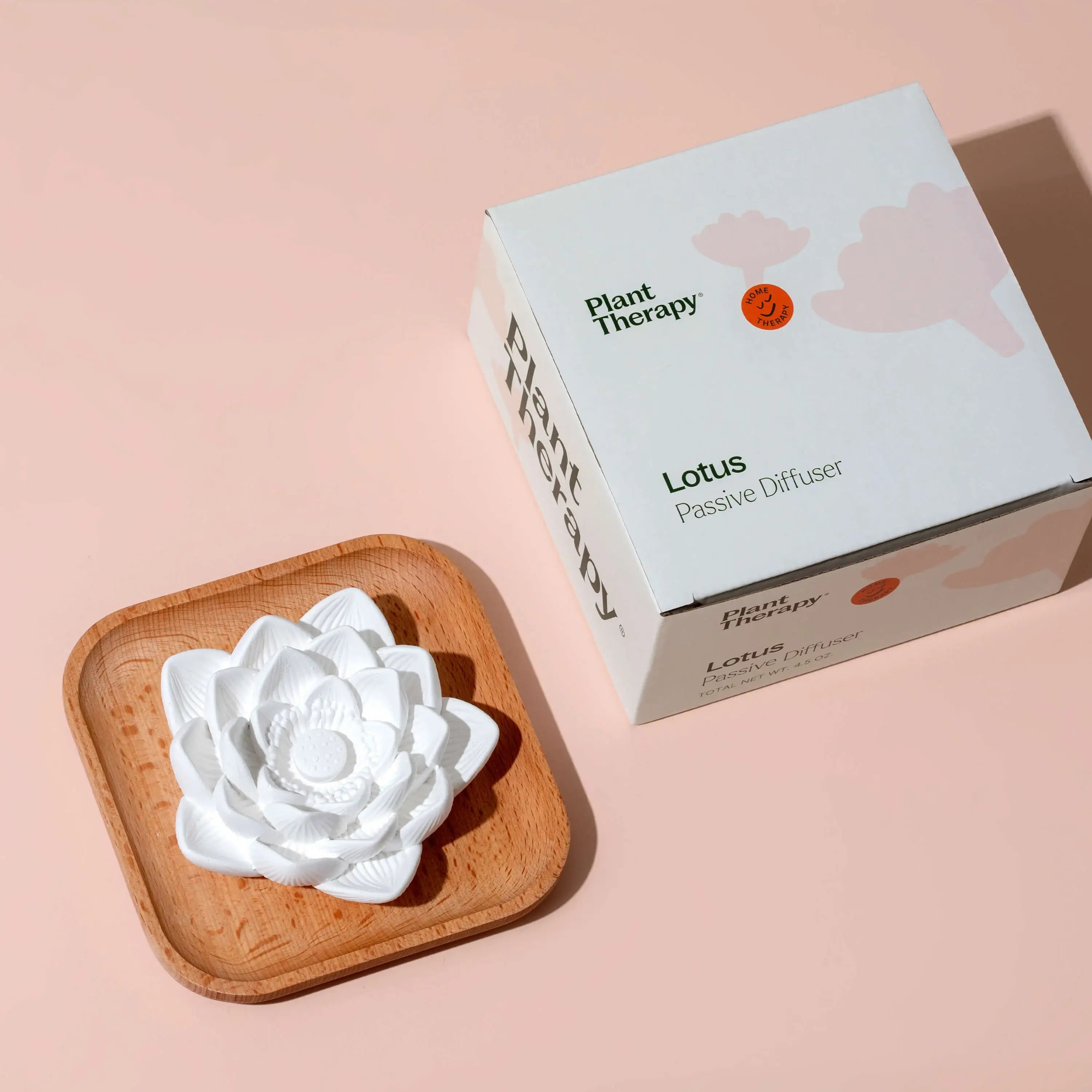 White lotus-shaped diffuser on a wooden coaster with Plant Therapy packaging on a pink background