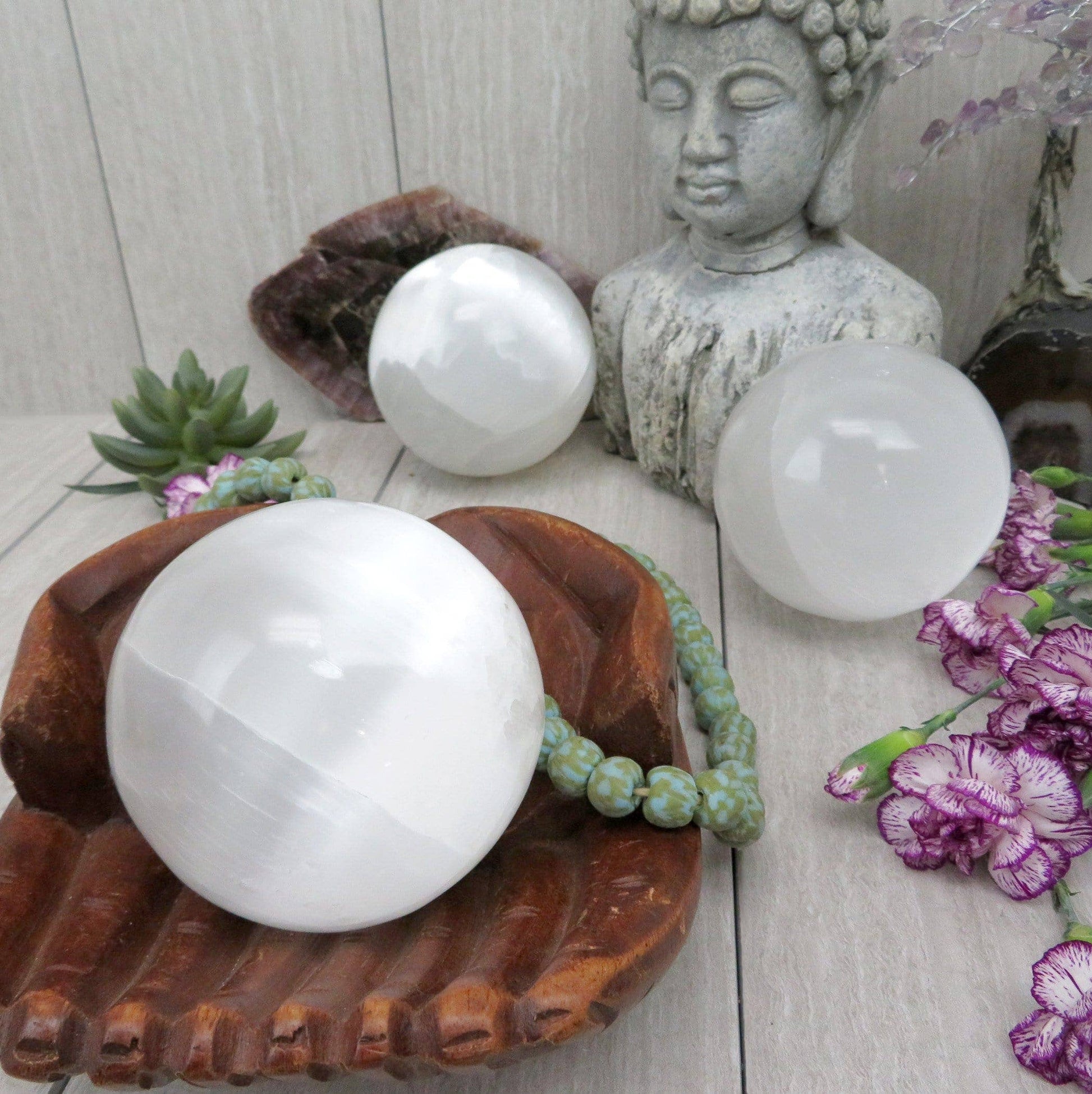 Three white spherical objects on a wooden surface with a Buddha statue and decorative elements.