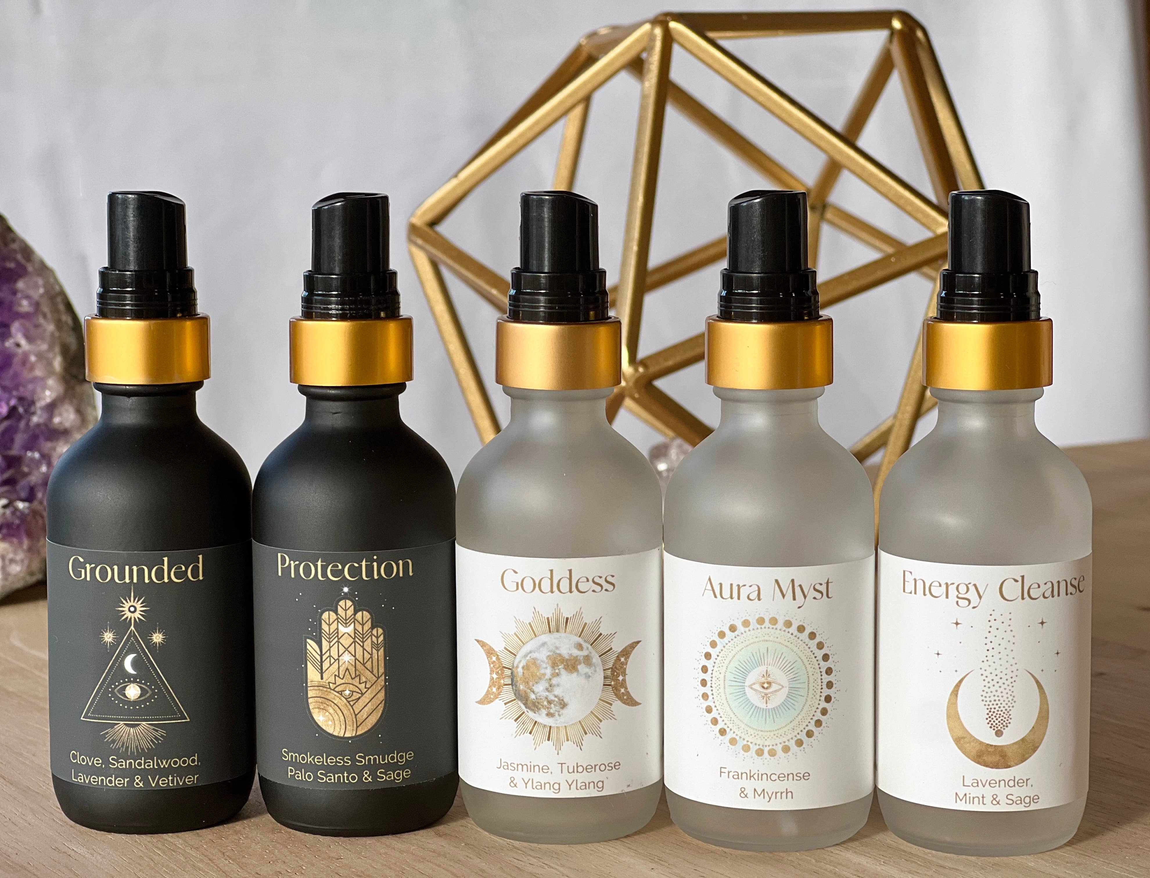 Five bottles with black and gold caps on a wooden surface, with geometric decor in the background.