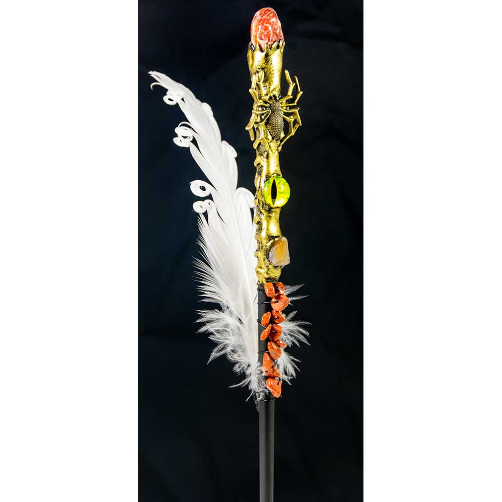 Decorative staff with gold spider, white feathers, and red accents on a black background