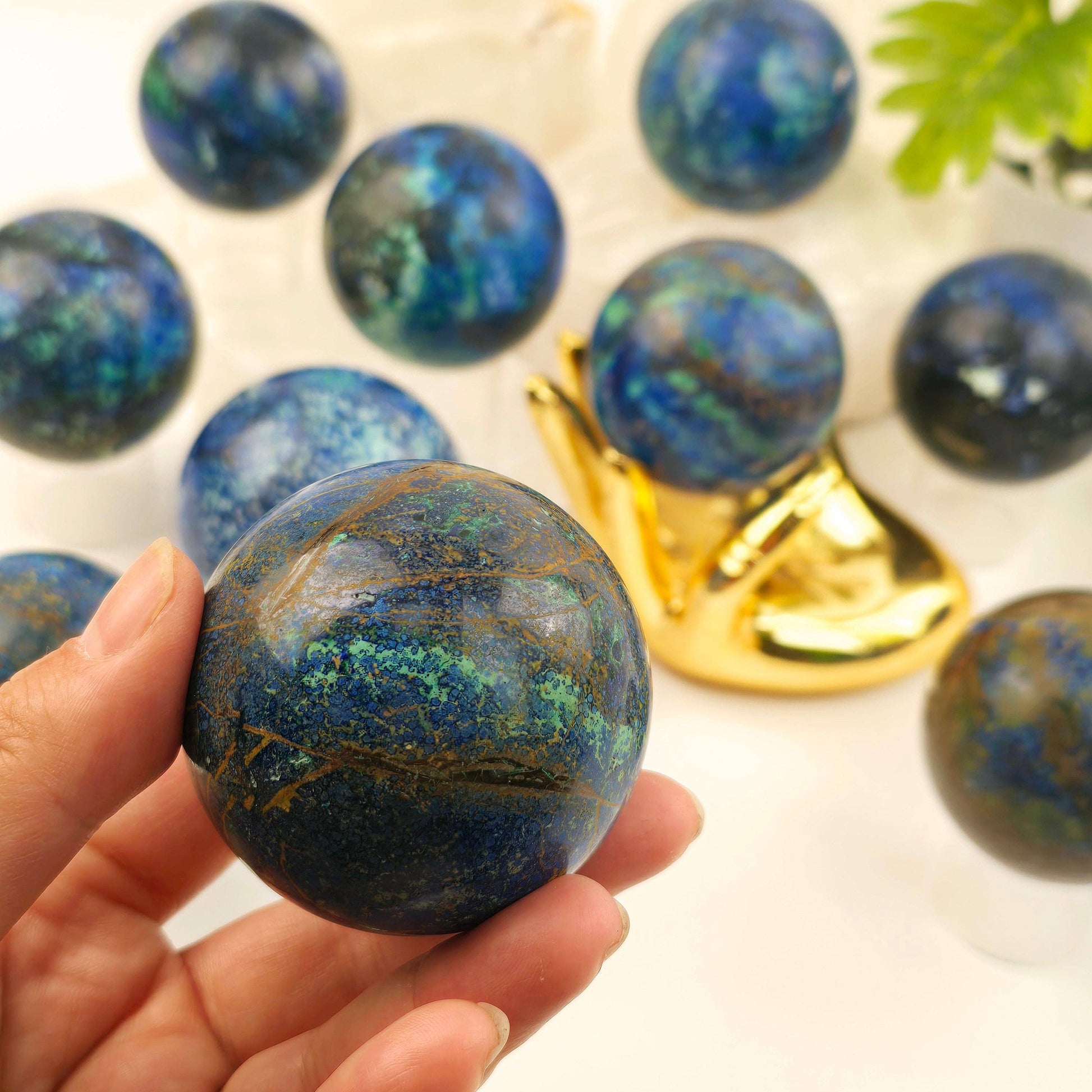 Blue marbled sphere held in a hand with more spheres on a reflective surface
