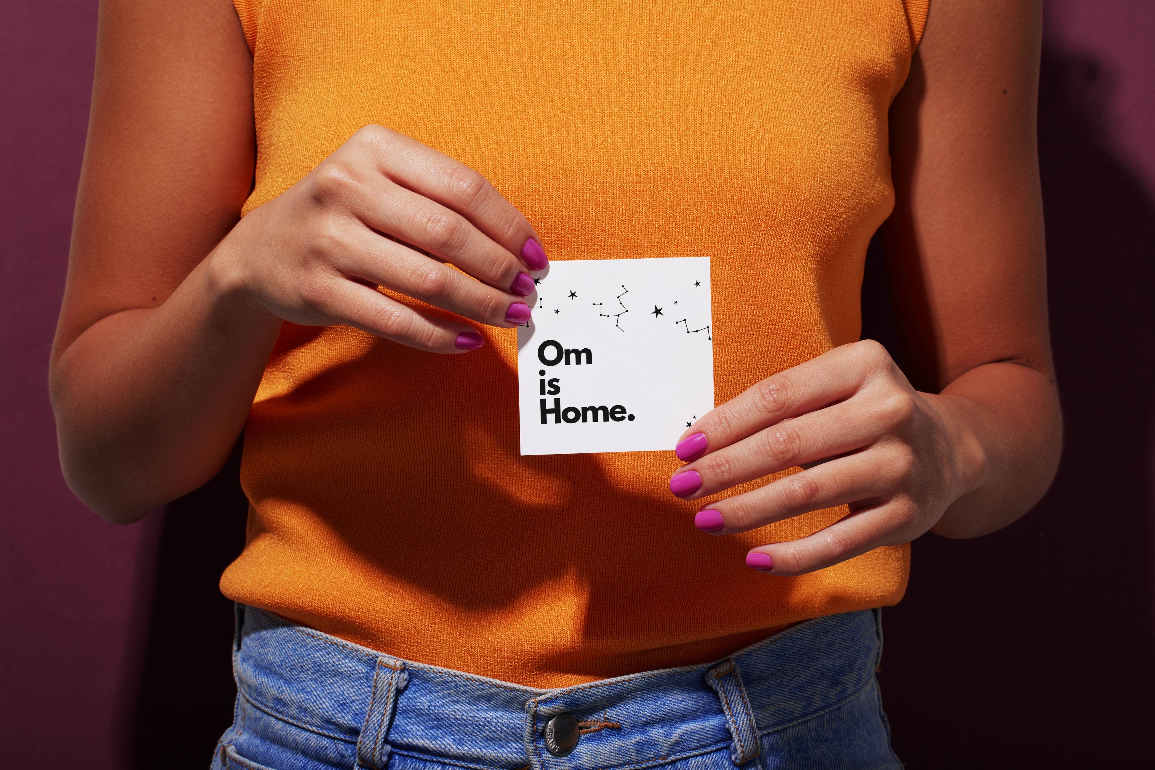 Person holding a card with 'Om is Home.' text against a purple background - JOY - Journey Of You - Spiritual, Holistic, Empowering