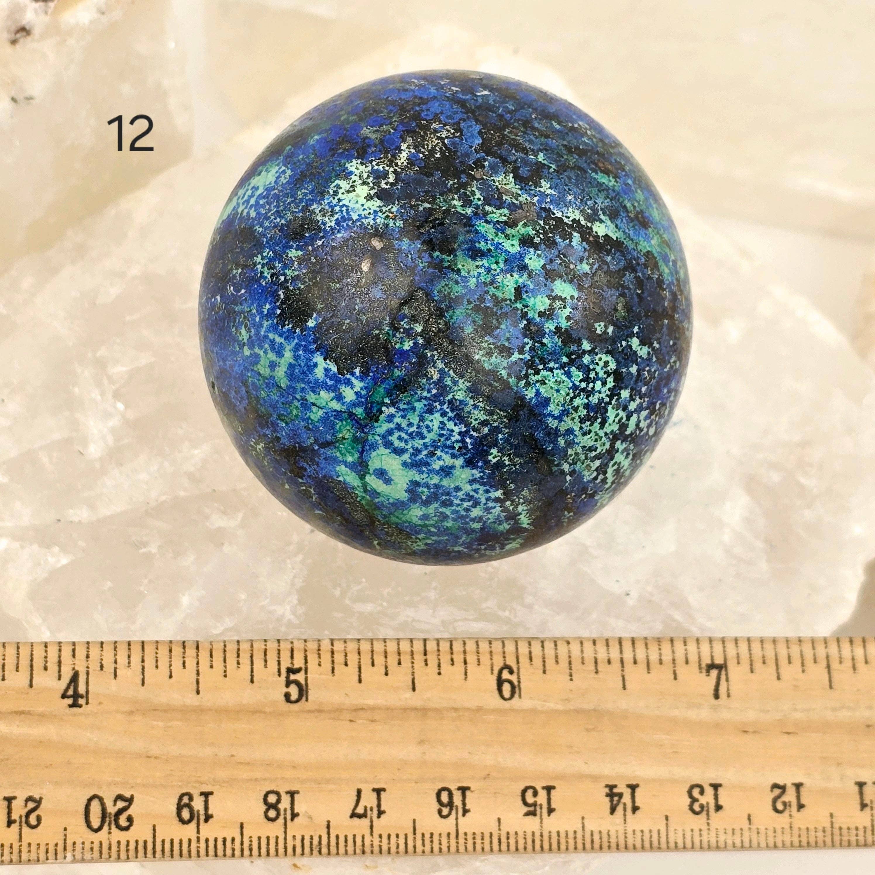 Blue and green marbled sphere on a white background with a ruler for scale.