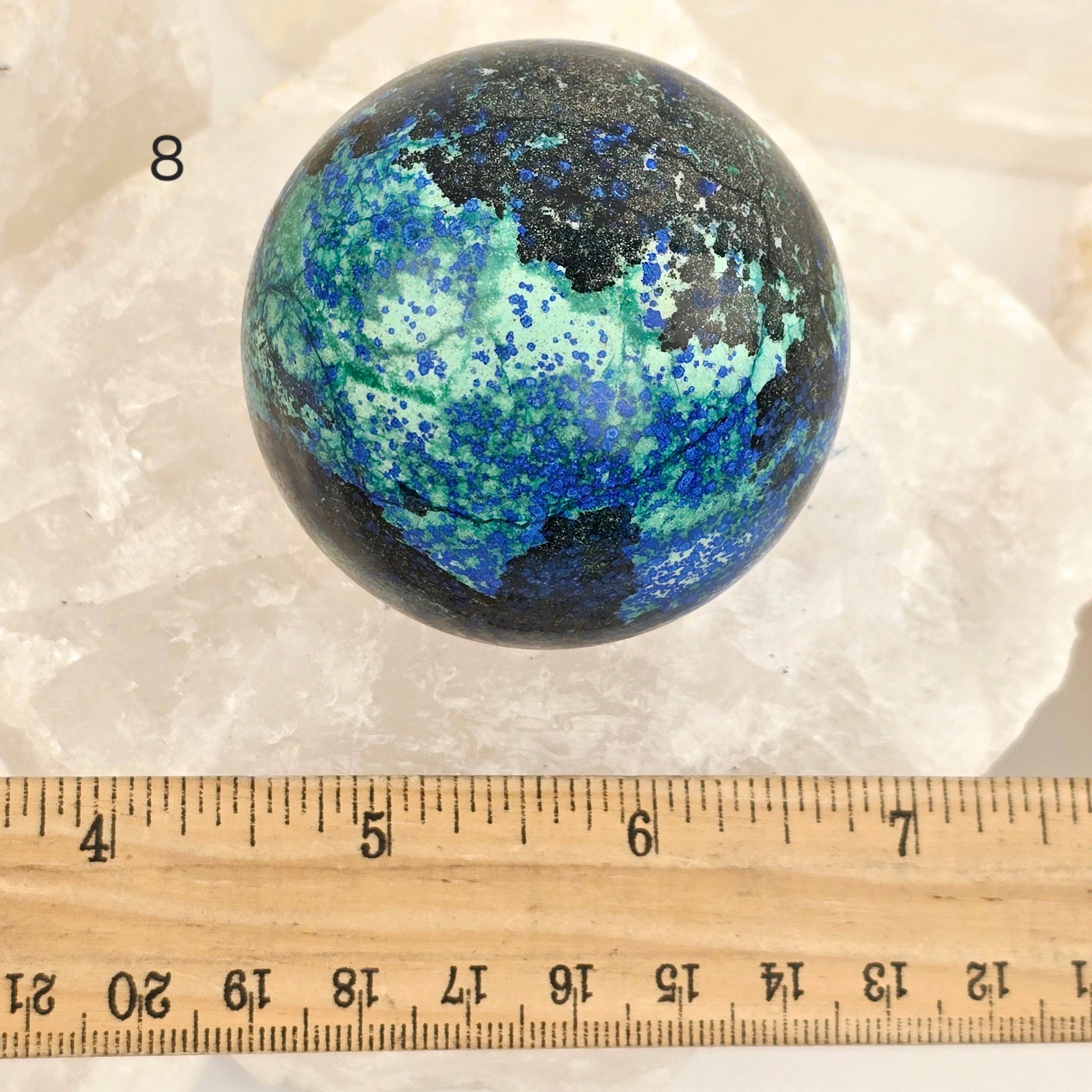 Multicolored marbled sphere on a textured surface with a ruler for scale.