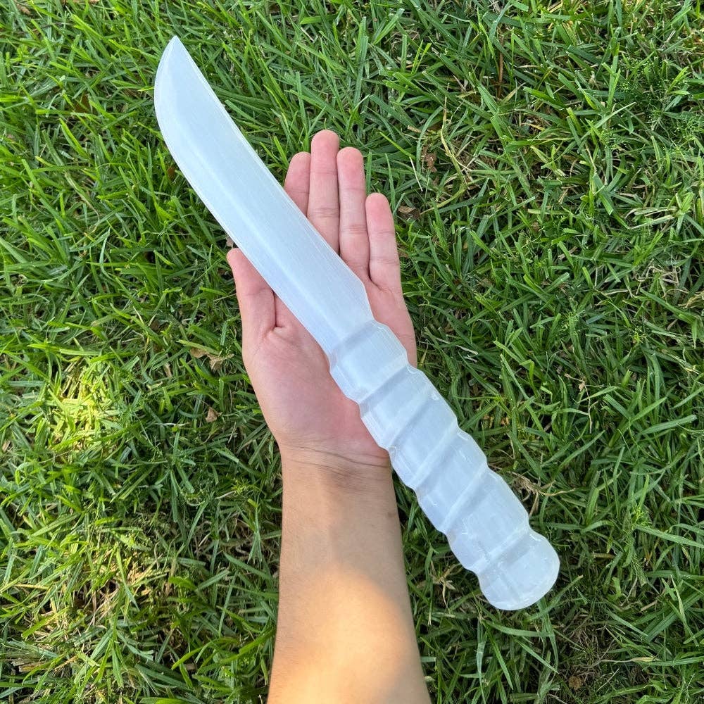 Hand holding a large white knife against a grass background