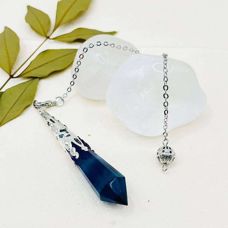 Necklace with a blue pendant on a white surface with green leaves