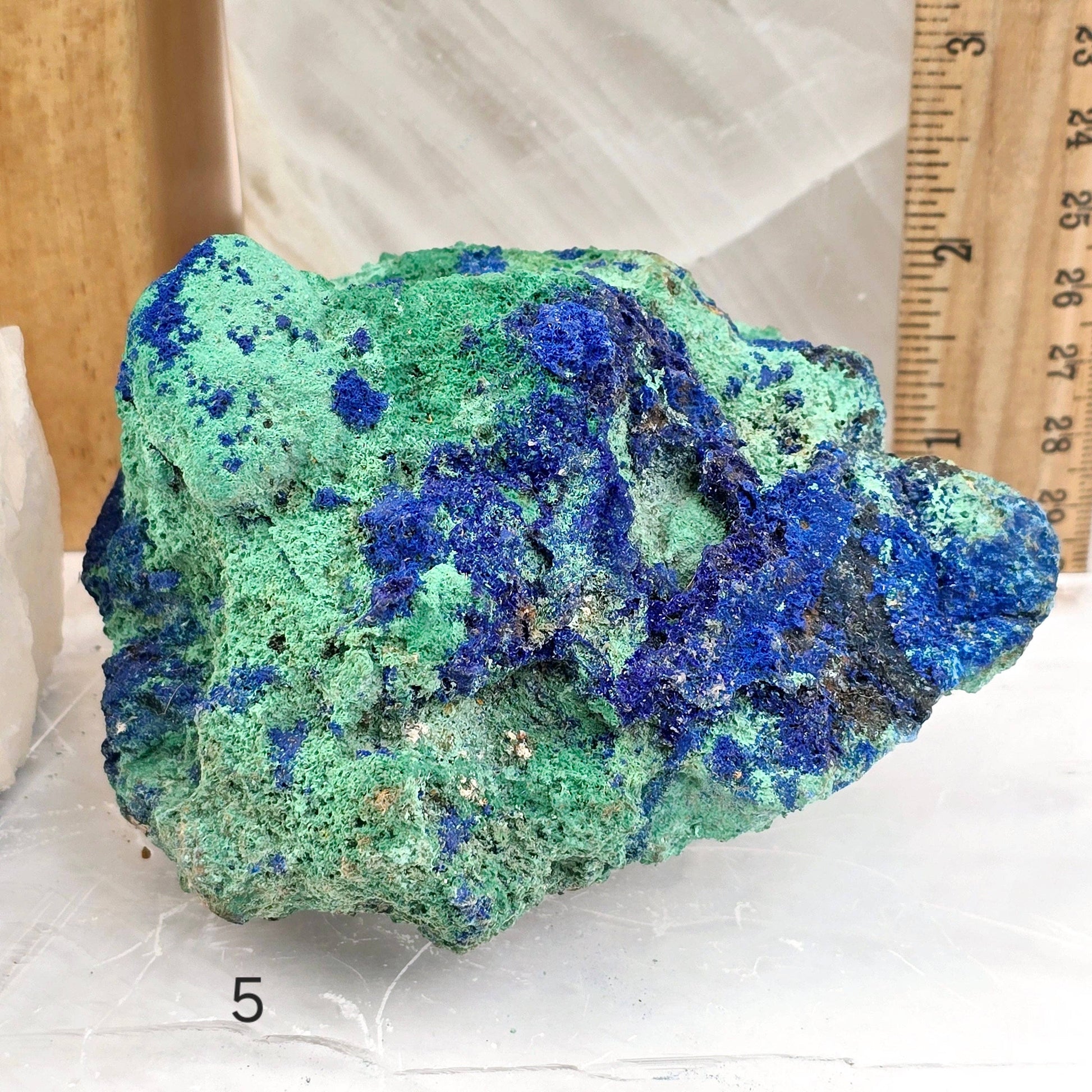 Green and blue mineral specimen with a ruler for scale on a white background