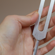 Hand holding a metal tuning fork against a neutral background