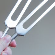 Metallic fork held by a hand against a gray background