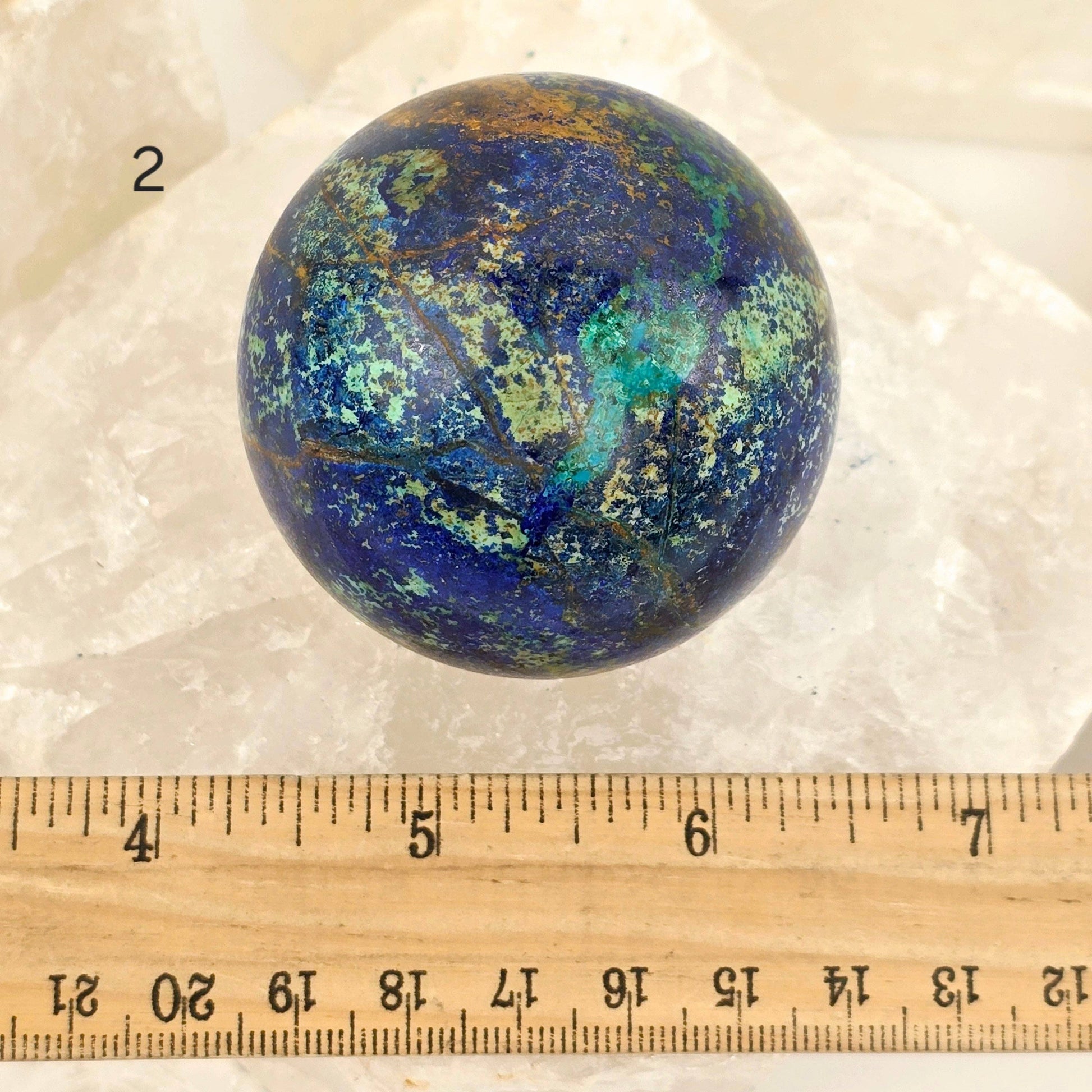 Marble-like sphere with blue and green patterns on a white background, measured against a ruler.