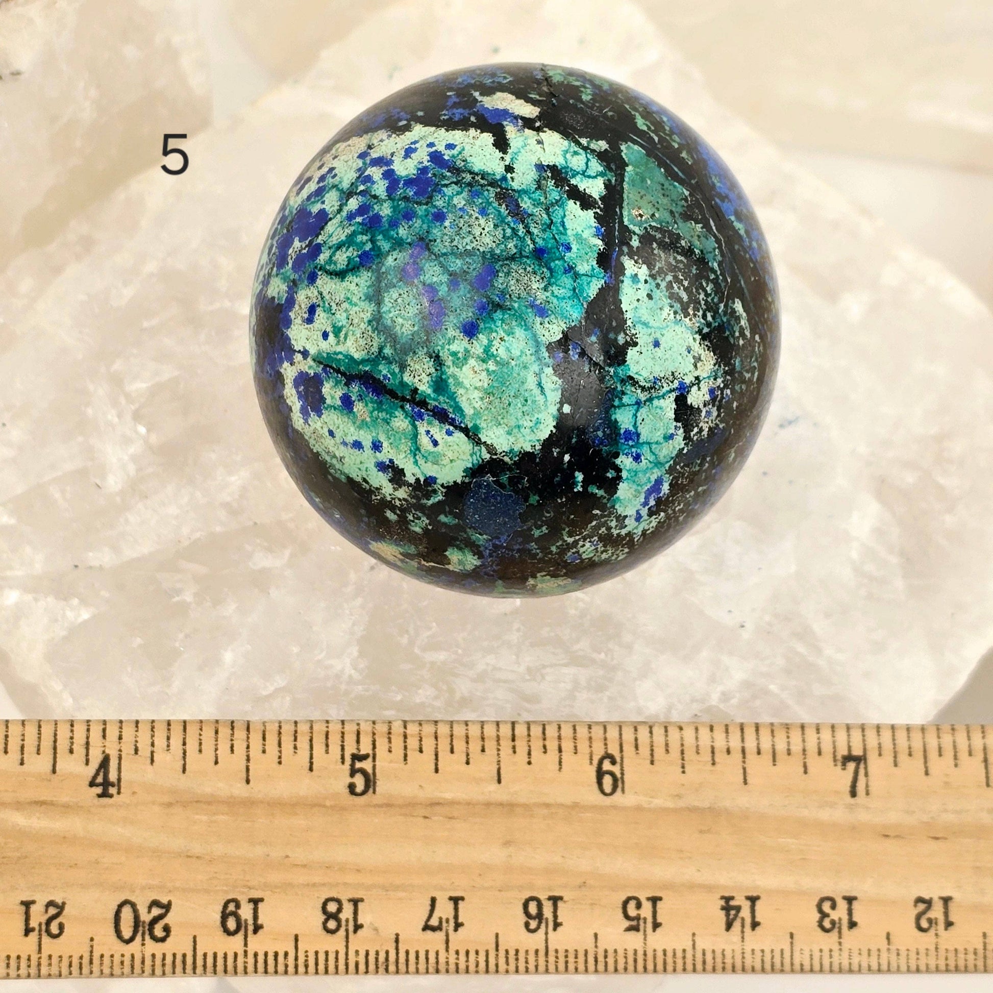 Marbled stone sphere with a ruler for scale on a white background