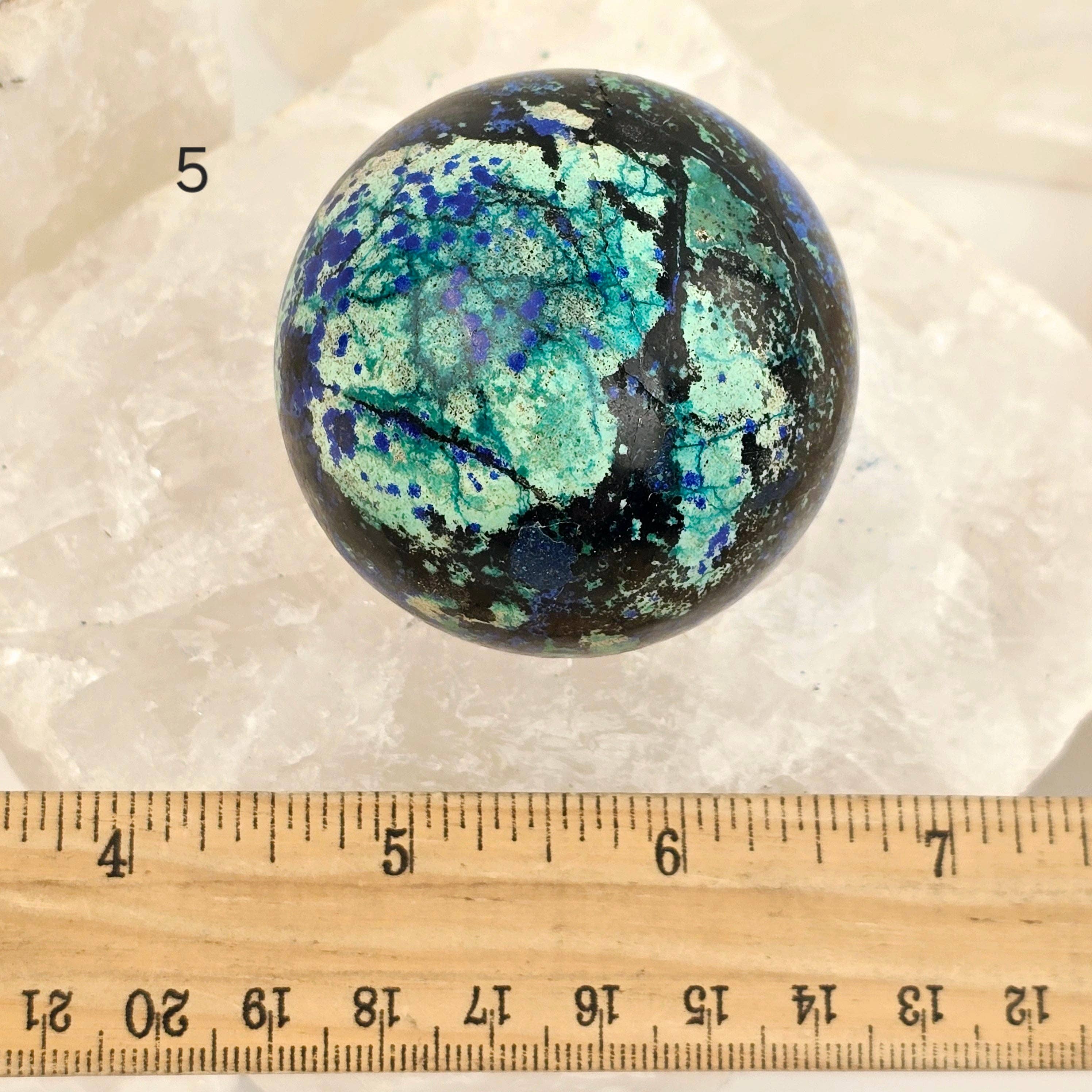 Marbled stone sphere with a ruler for scale on a white background