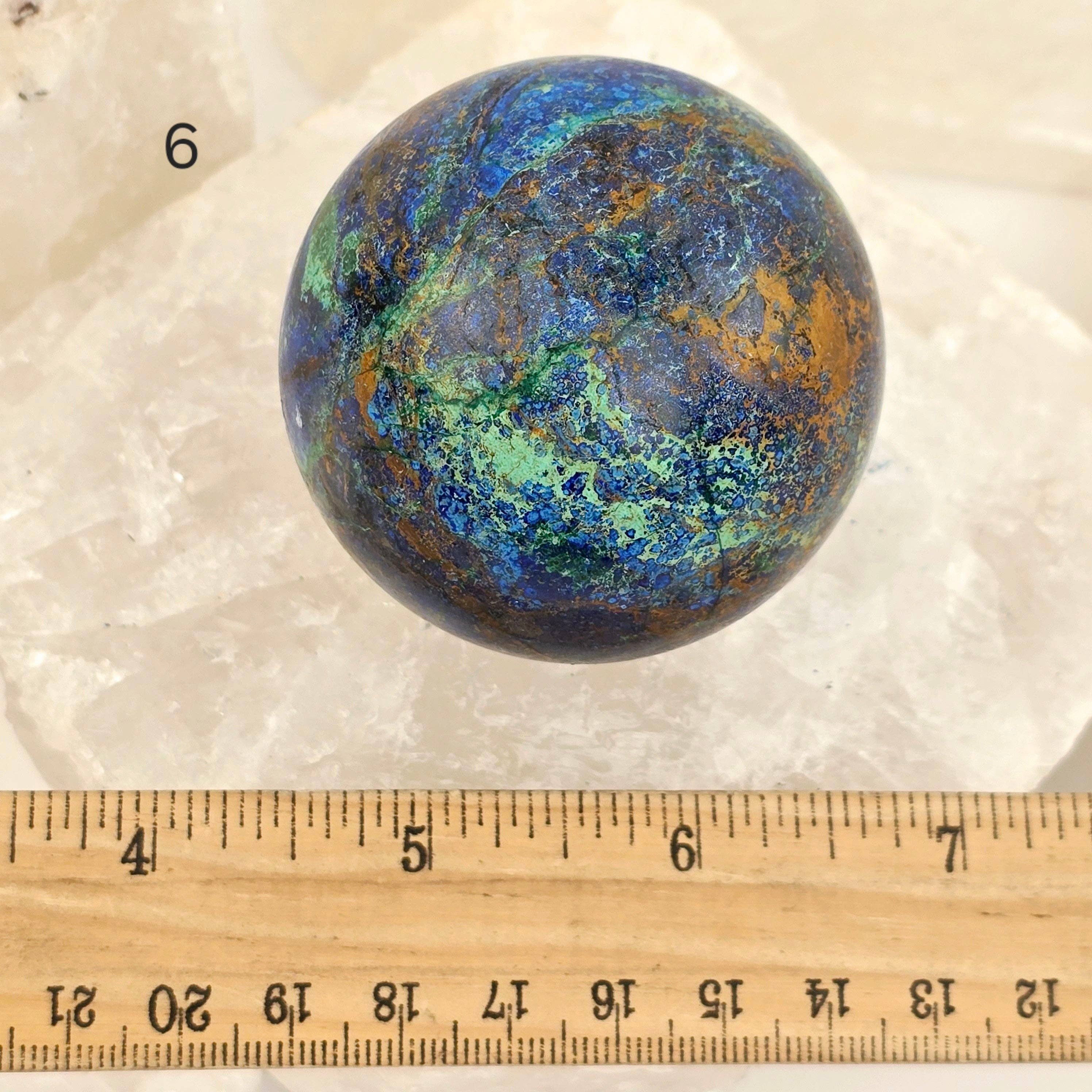 Multicolored spherical stone on a white background with a ruler for scale.