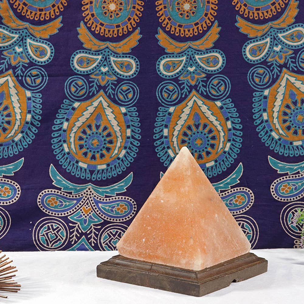 Pyramid-shaped salt lamp on a wooden base against a decorative purple fabric background
