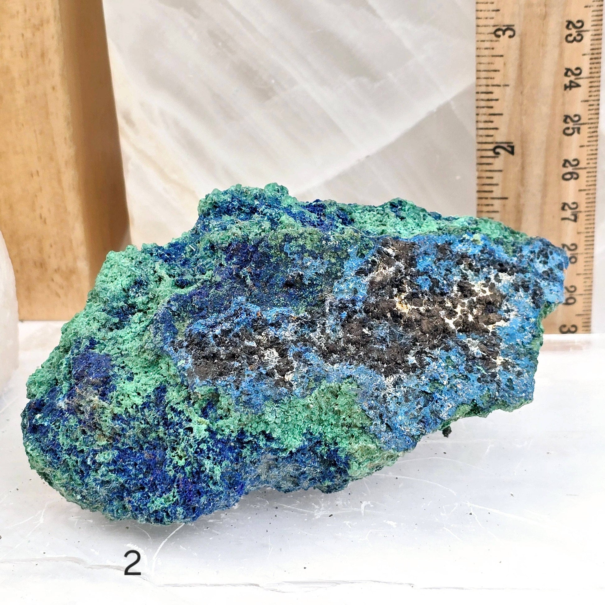 Blue and green mineral specimen on a white surface with a ruler for scale.