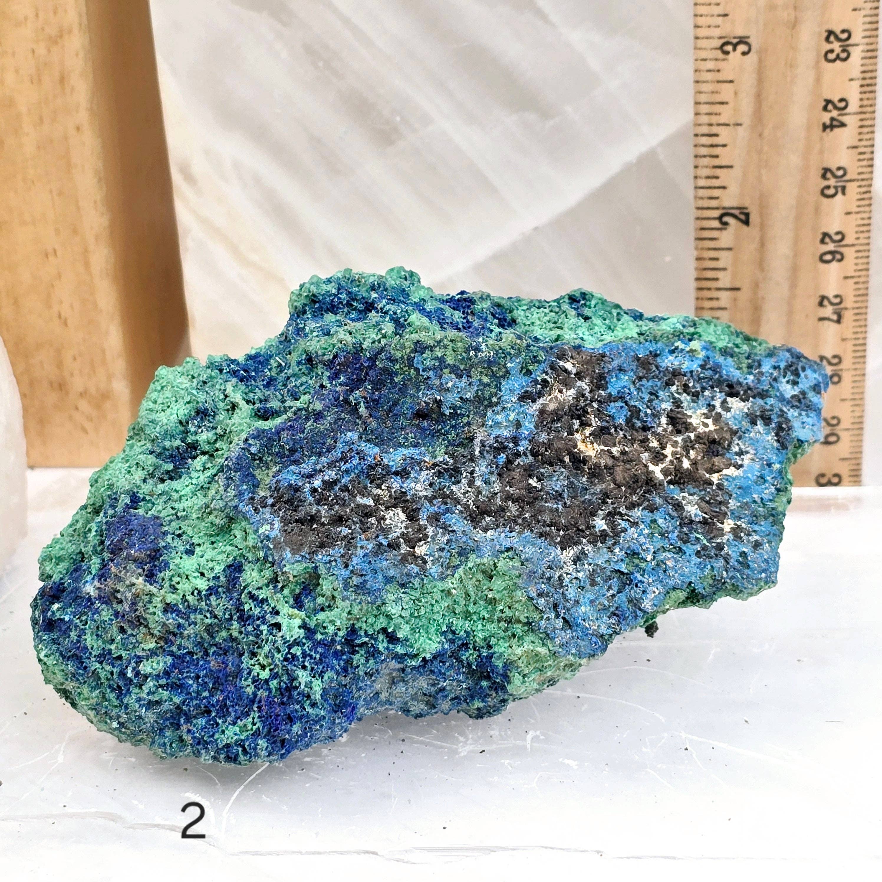 Blue and green mineral specimen on a white surface with a ruler for scale.