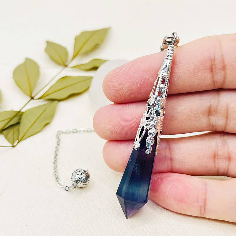 Hand holding a blue crystal pendant with silver detailing on a light background