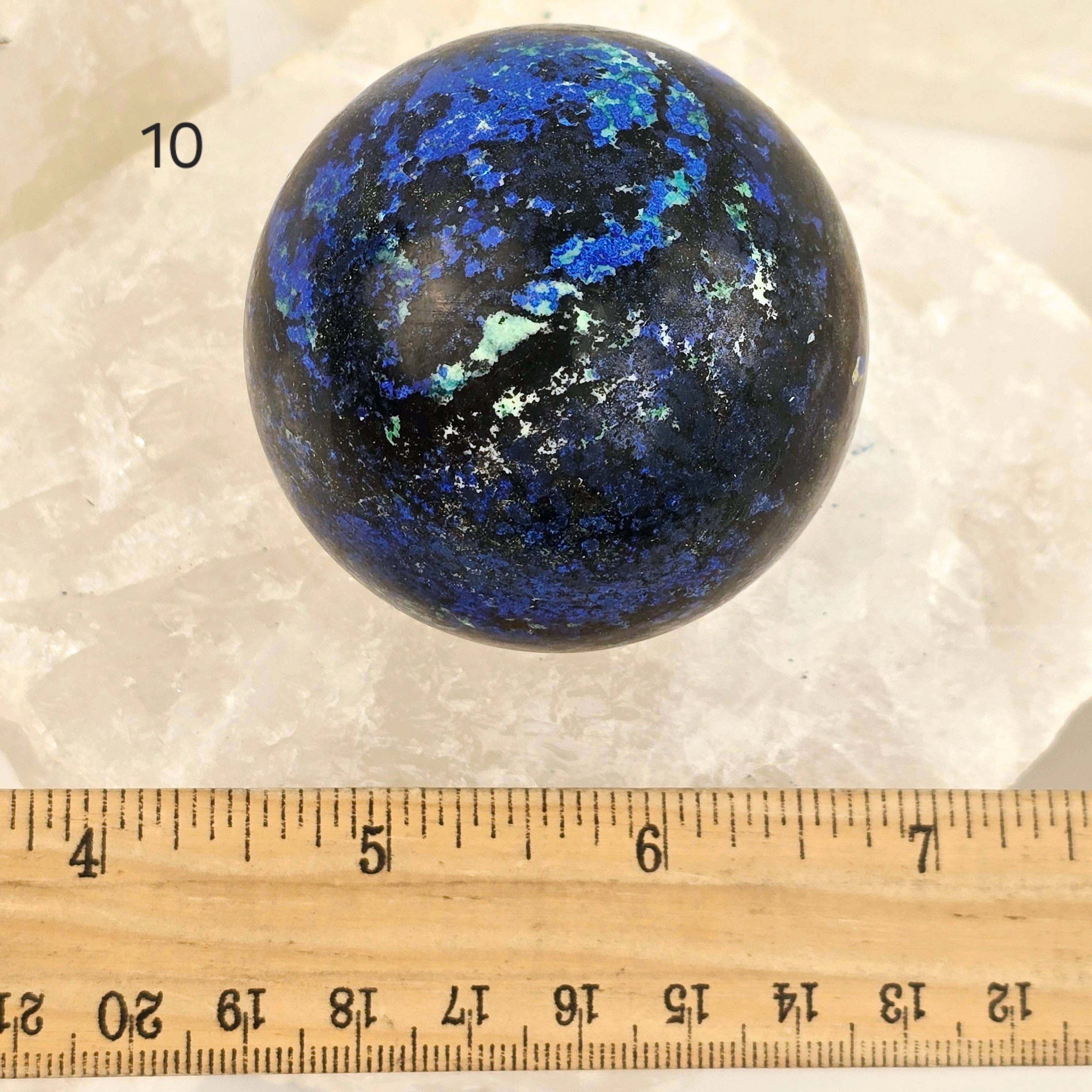 Blue and black marbled sphere on a white background with a ruler for scale.