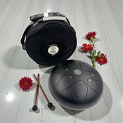 Black handpan with drumsticks and flowers on a light wooden surface