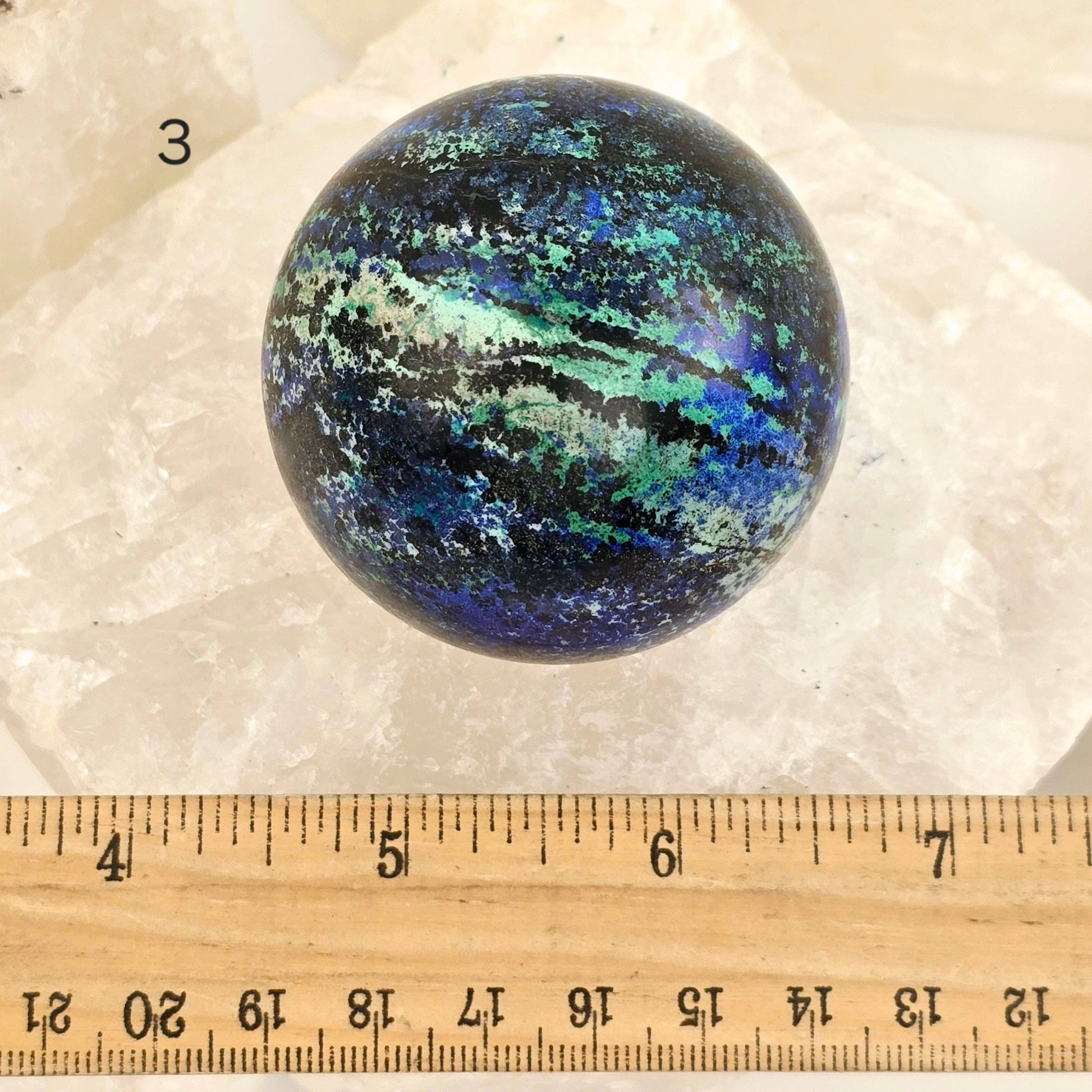 Multicolored spherical stone on a white background with a ruler for scale.