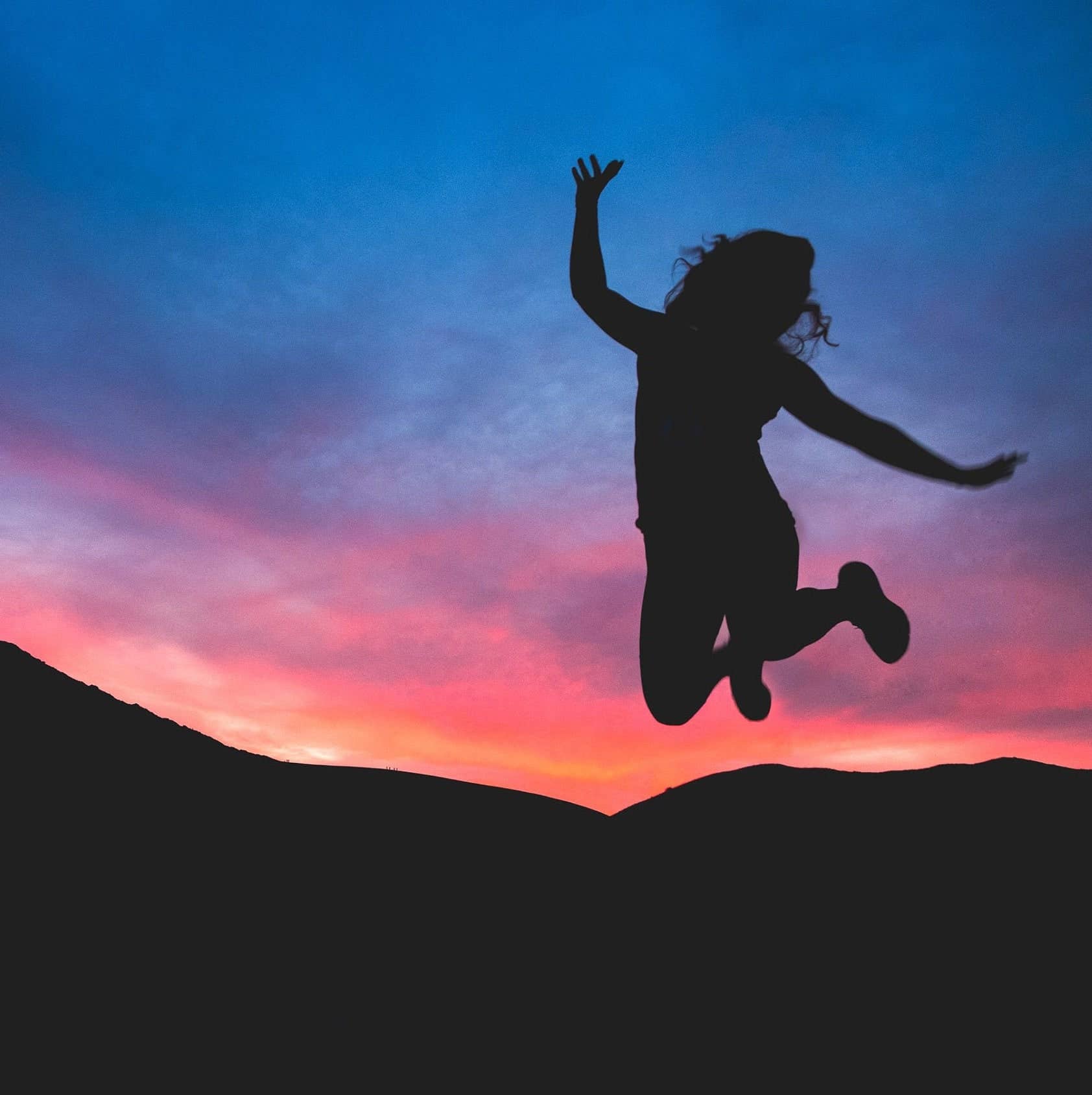 Person jumping against a colorful sunset sky - JOY - Journey Of You - Spiritual, Holistic, Empowering