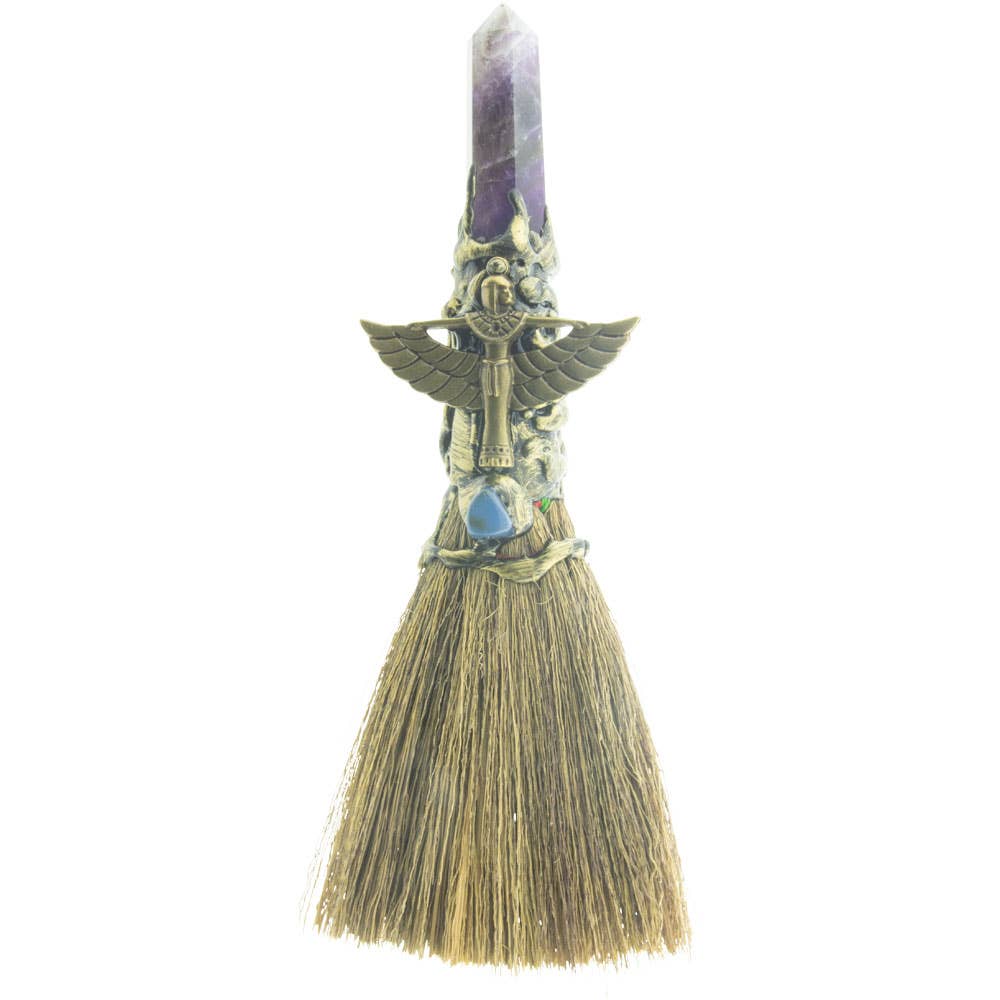 A decorative gemstone wicca broom with an amethyst handle, gold Isis figure, and natural bristles.