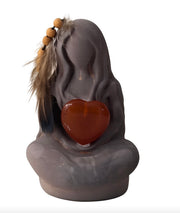 Grey stylized statue of a seated figure holding a red polished heart stone.