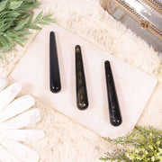 Three golden sheen obsidian wands arranged on a white surface, with a white glove and decorative items in the background.