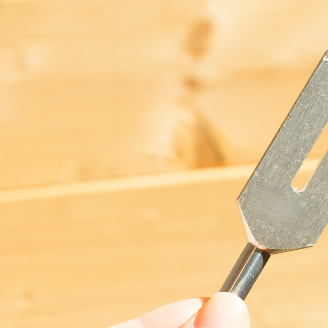 222 Hz Unweighted Tuning Fork: Metal tool held by a hand against a blurred yellow background